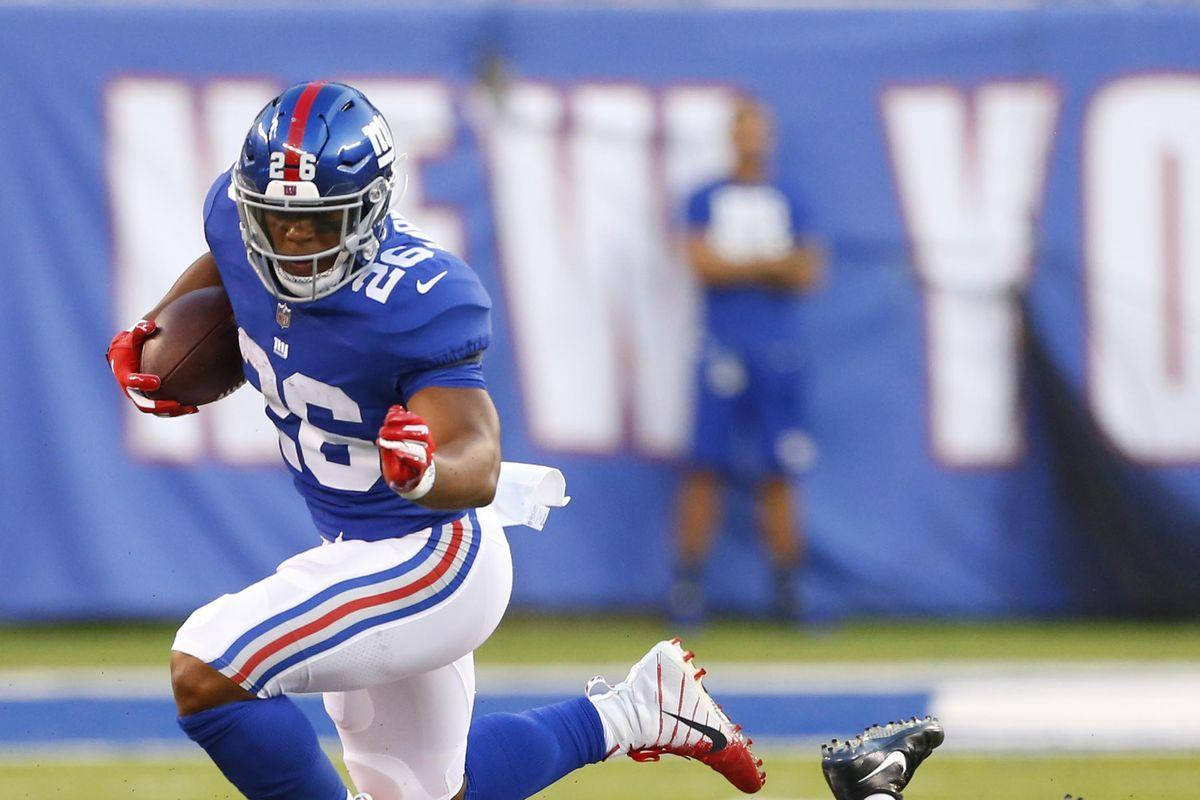 Saquon Barkley 桌布 壁紙 — 一名紐約巨人隊的美式足球員身穿藍白球衣，在日間比賽中持球衝刺。