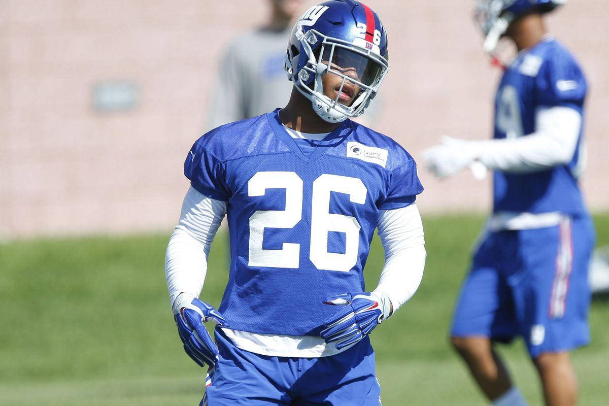 Saquon Barkley 桌布 壁紙 — 一名紐約巨人隊美式足球員身穿藍色26號球衣，在陽光明媚的草地上練習。