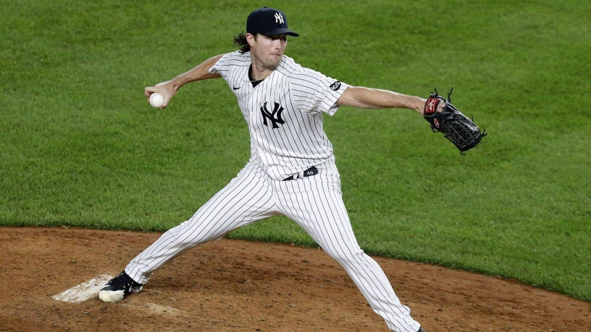 Gerrit Cole 桌布 壁紙 — 一名紐約洋基隊投手在球場燈光下，於充滿活力的綠色草地和棕色泥土的棒球投手丘上投球中。
