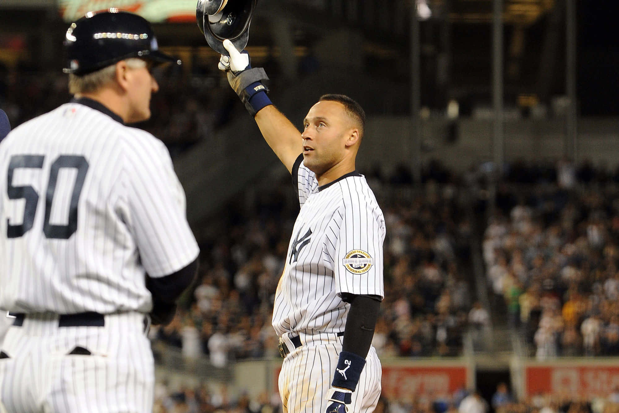 Derek Jeter 桌布 壁紙 — 一名紐約洋基隊棒球選手在球場燈光下高舉頭盔，球迷歡呼慶祝勝利。