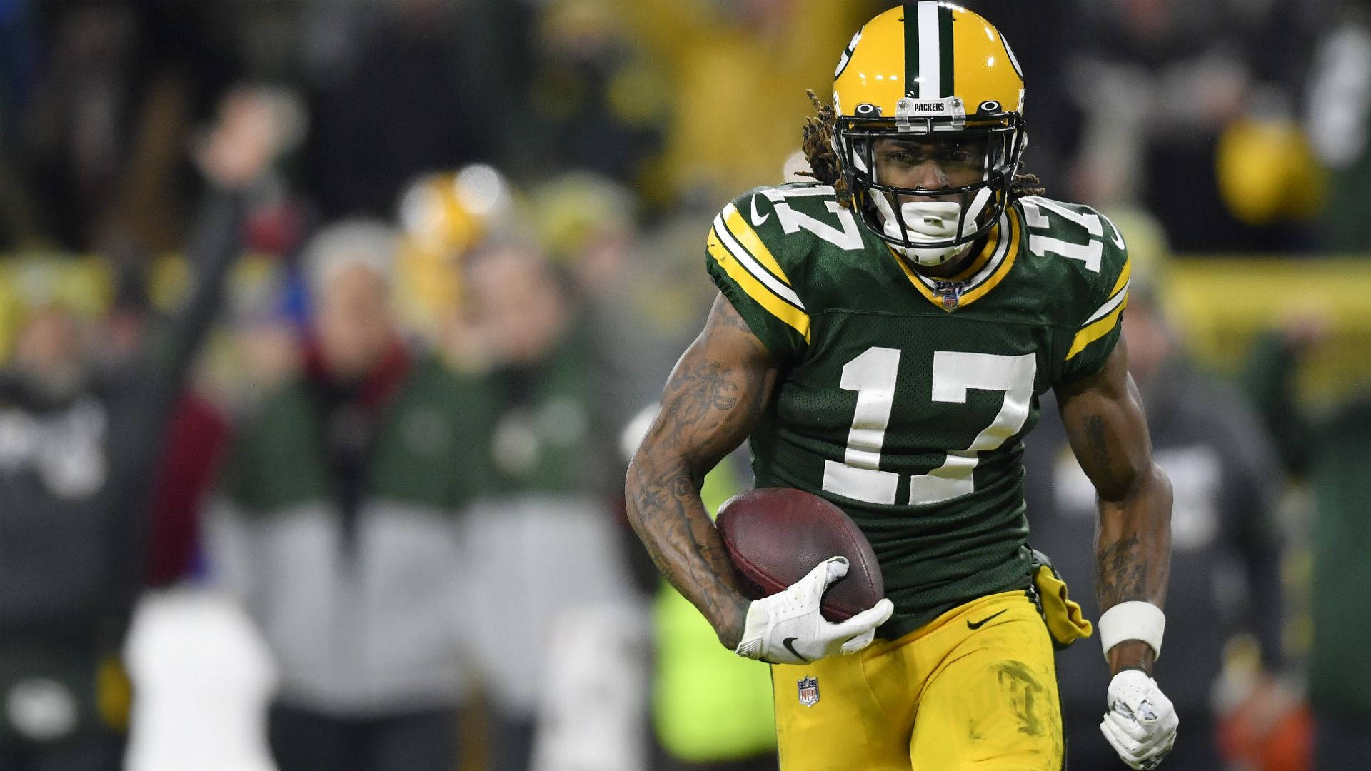 Davante Adams 桌布 壁紙 — 一名綠灣包裝工美式足球員身穿綠色和金色制服，在夜間比賽中於球場燈光下持球奔跑。