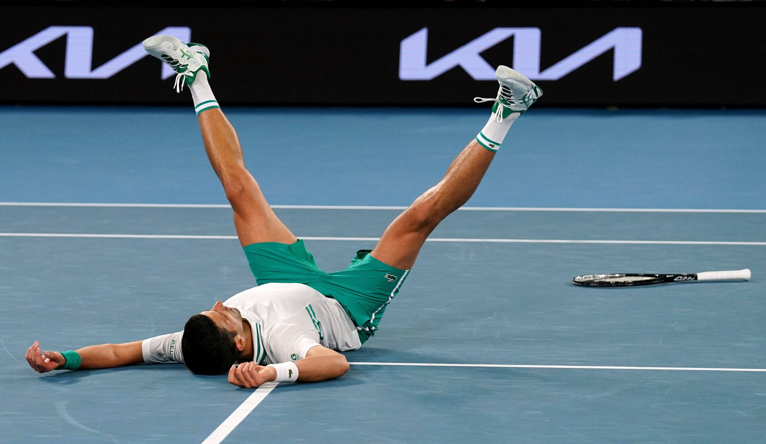 Australian Open 桌布 壁紙 — 一名網球運動員在慶祝時倒在藍色球場上，雙腿朝天，球拍被遺棄在旁邊。
