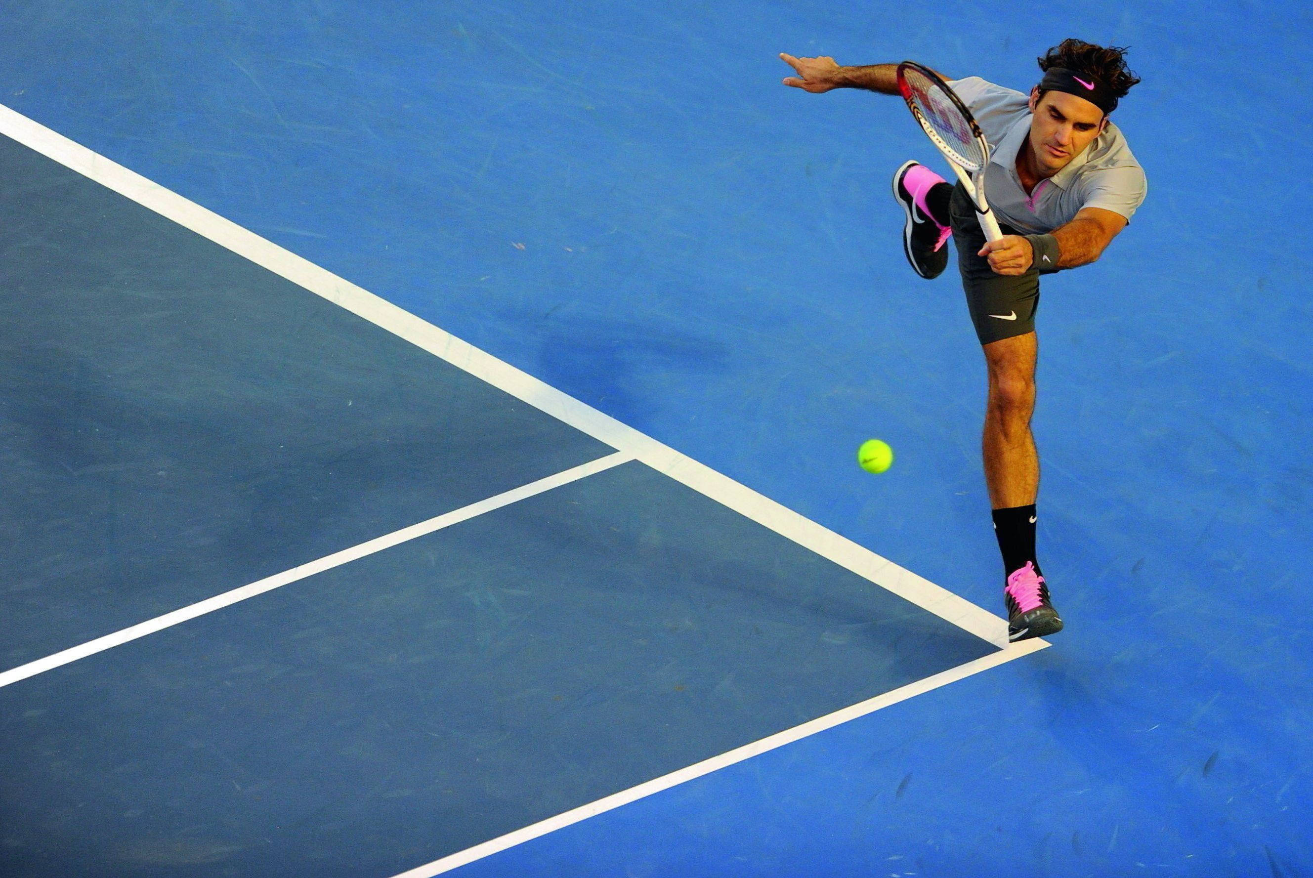 Australian Open 桌布 壁紙 — 一名網球選手在藍色球場上動態跳躍，以高度專注擊打明亮的黃色球。