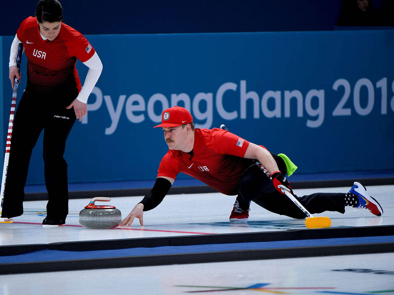 Olympics 桌布 壁紙 — 一名美國冰壺運動員在冰上滑行石頭，隊友在平昌2018冬奧會觀看。