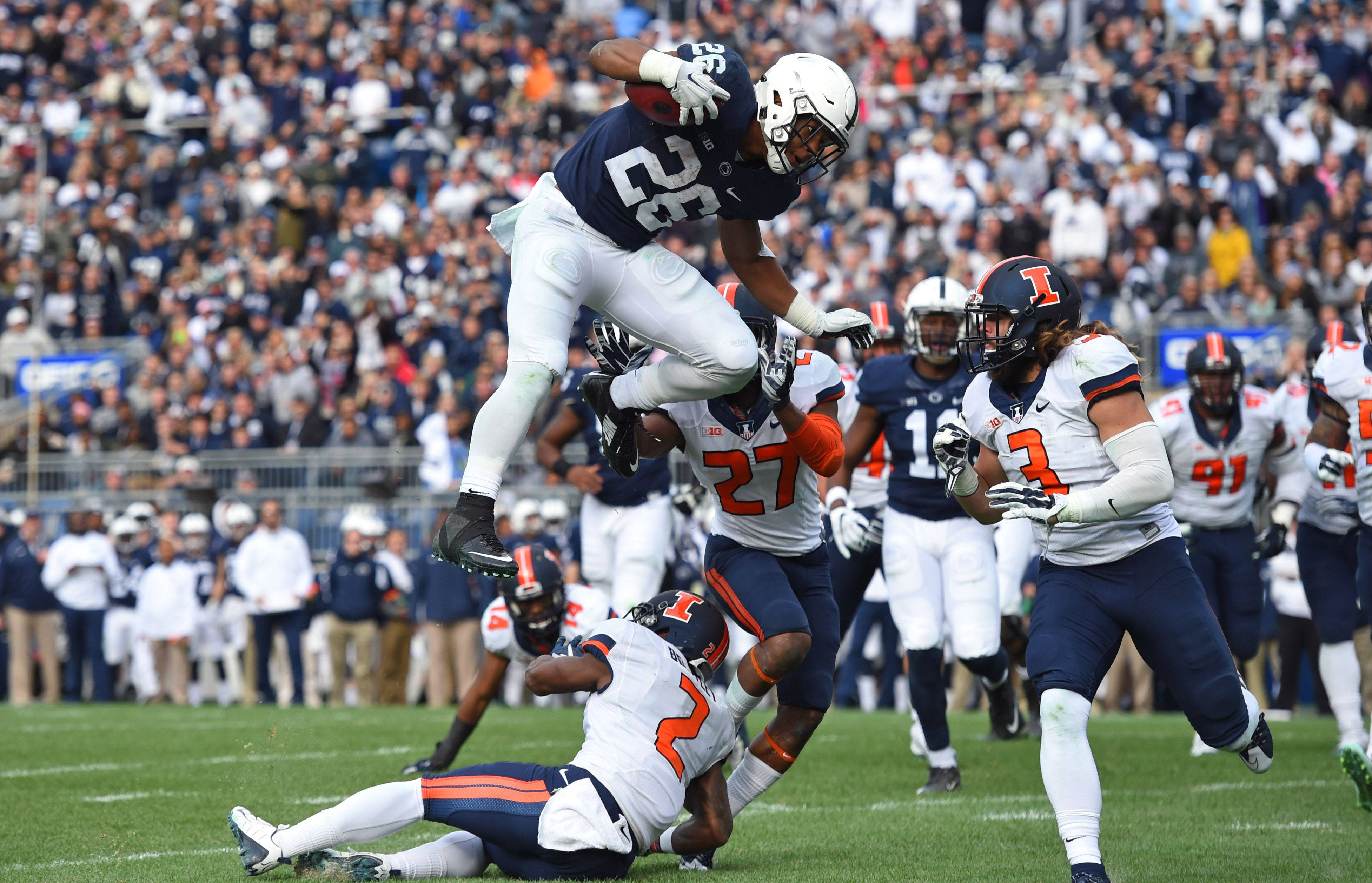 Saquon Barkley 桌布 壁紙 — 一名美式足球員在擠滿觀眾的體育館比賽中，跳起接球，防守球員正在逼近。