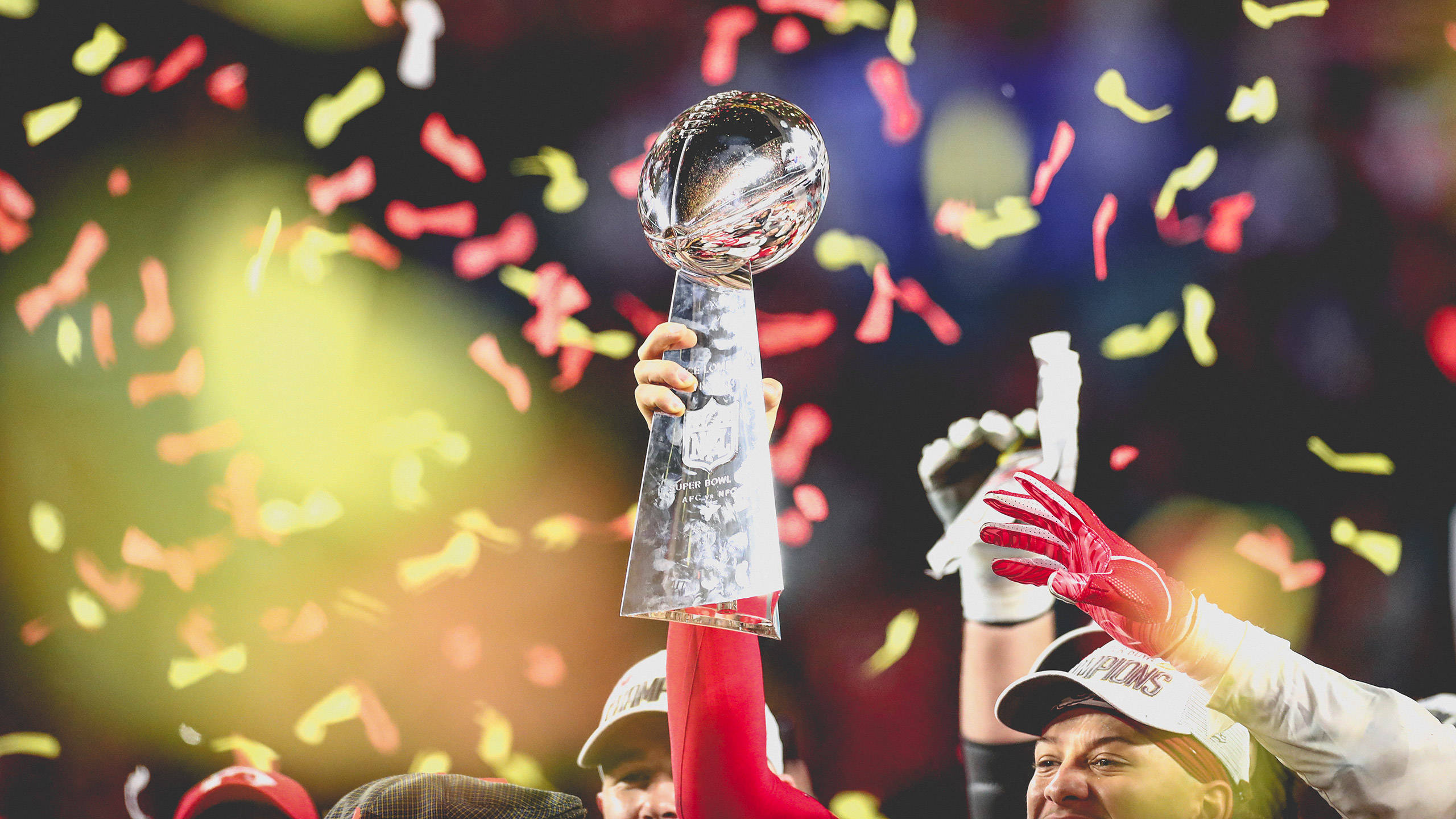 酋長 桌布 壁紙 — 一名美式足球運動員勝利地高舉閃亮的隆巴迪獎盃，彩色紙屑在體育館慶祝活動中如雨般落下。