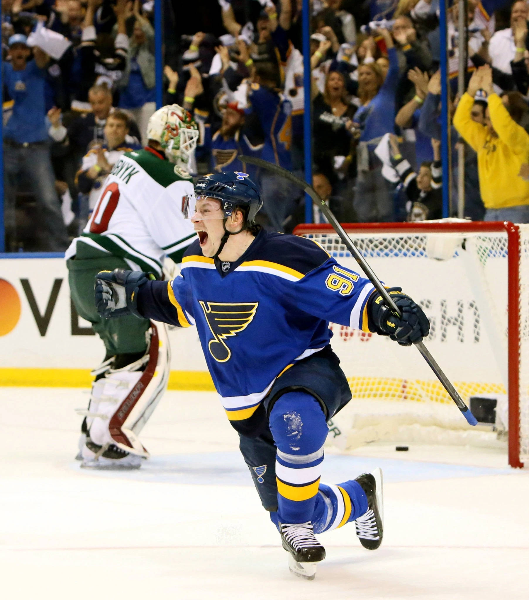 St Louis Blues 桌布 壁紙 — 一名聖路易斯藍調冰球球員身穿藍色球衣，在冰上張開雙臂慶祝進球，身後觀眾歡呼。