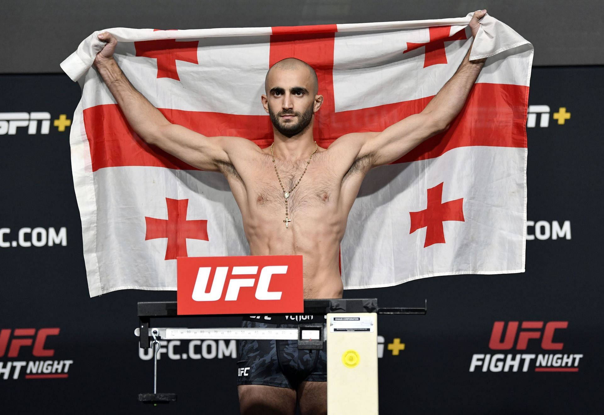 Champion 桌布 壁紙 — 一名肌肉發達、光頭、留鬍子的拳手在UFC稱重活動中勝利地舉起喬治亞國旗。