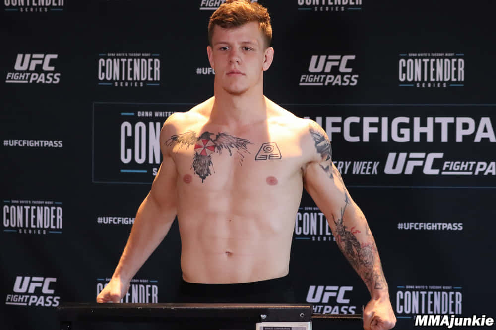 UFC 桌布 壁紙 — 一名肌肉發達、有刺青的男拳手在UFC稱重時赤裸上身，背景為品牌標誌。