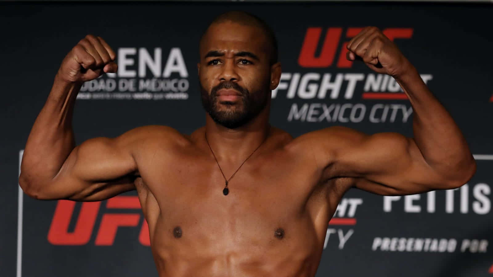 UFC 桌布 壁紙 — 一名肌肉發達、赤裸上身的拳手在墨西哥城的UFC稱重活動中，表情嚴肅地彎曲手臂。