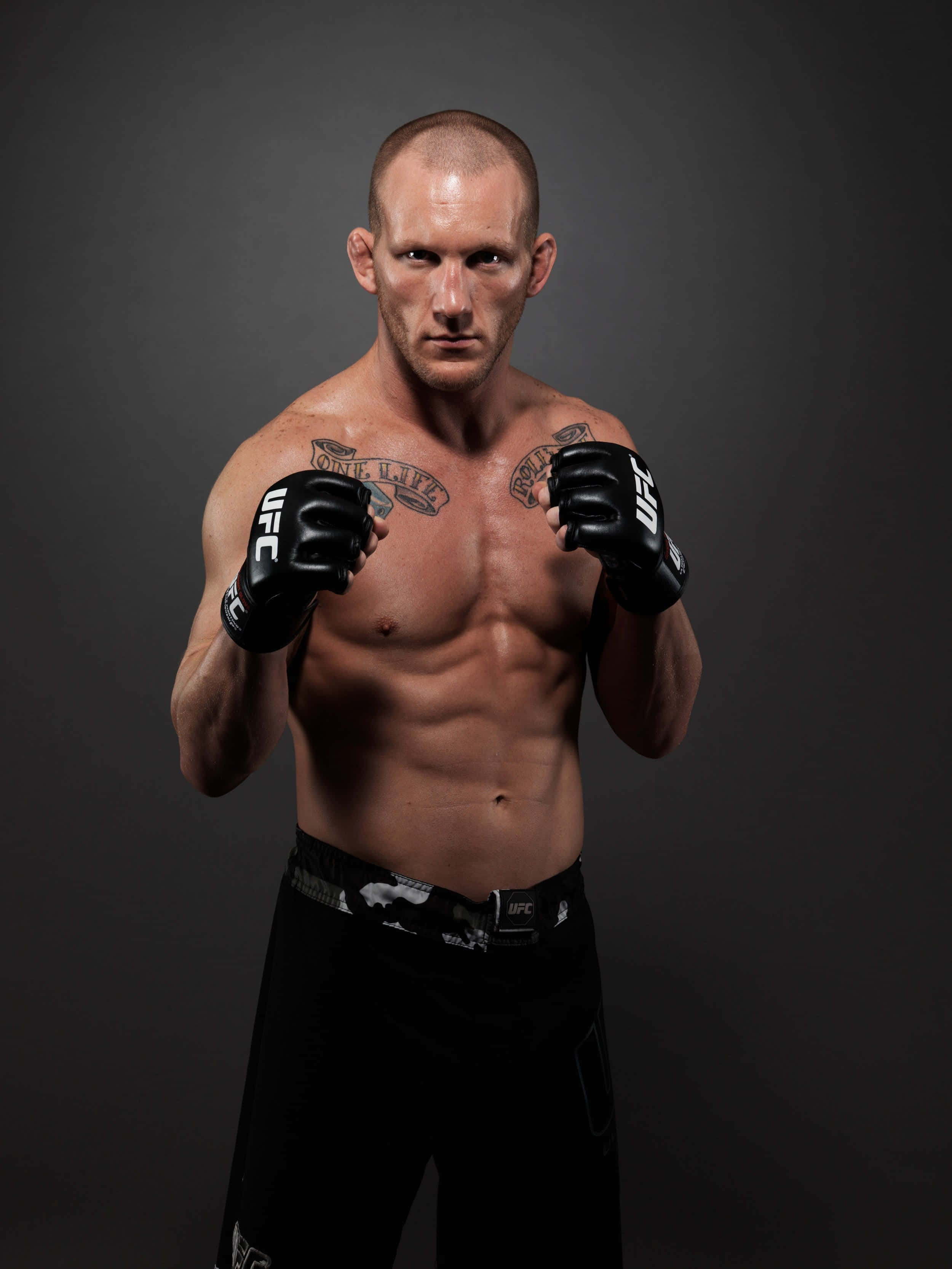 Fight 桌布 壁紙 — 一名肌肉發達的UFC拳手，戴著黑色手套和穿著黑色短褲，在深灰色工作室背景前擺出戰鬥姿勢。