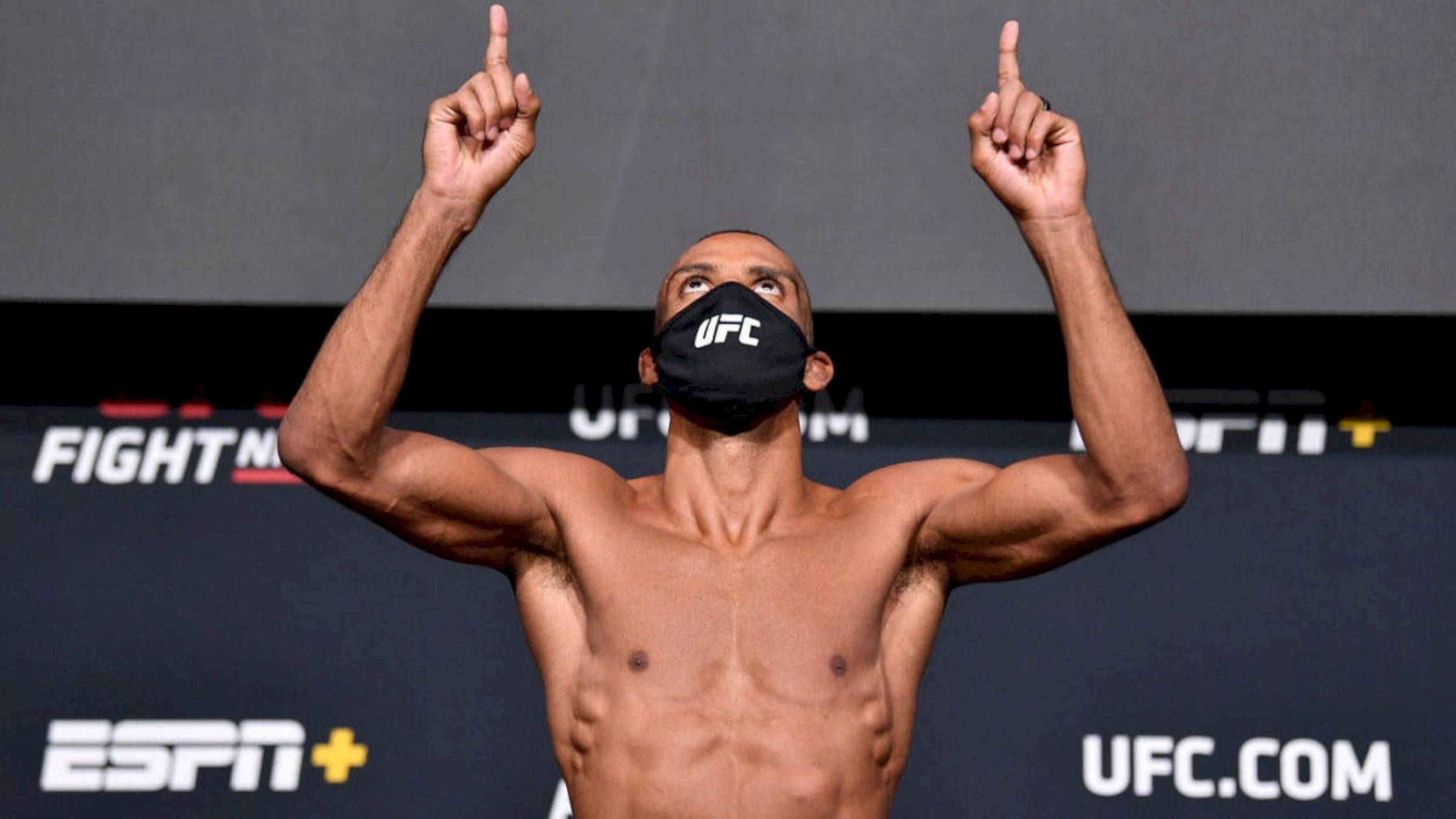 UFC 桌布 壁紙 — 一名肌肉發達的UFC拳手戴著黑色面罩，在品牌背景前勝利地舉起雙食指。