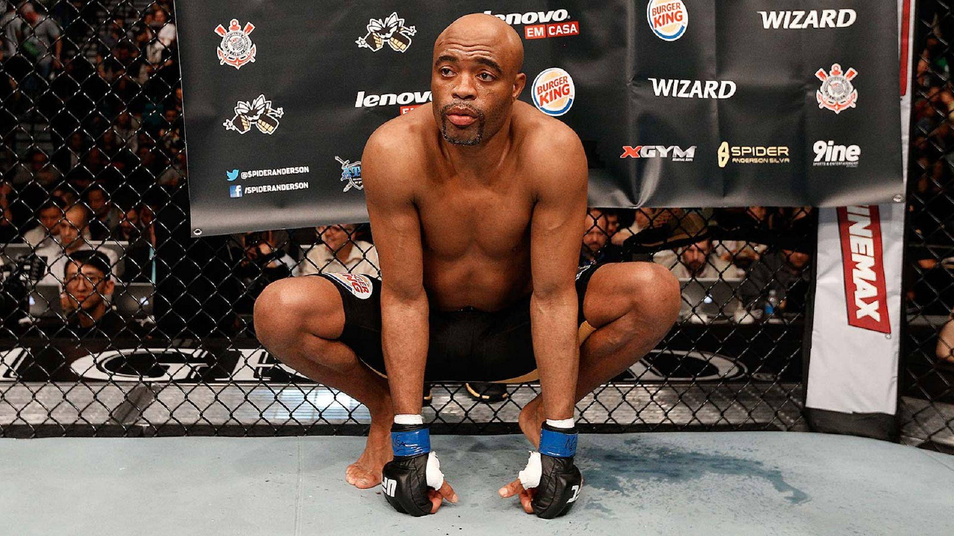 UFC 桌布 壁紙 — 一名肌肉發達的光頭拳手在身後有贊助商橫幅的MMA八角籠內蹲伏。