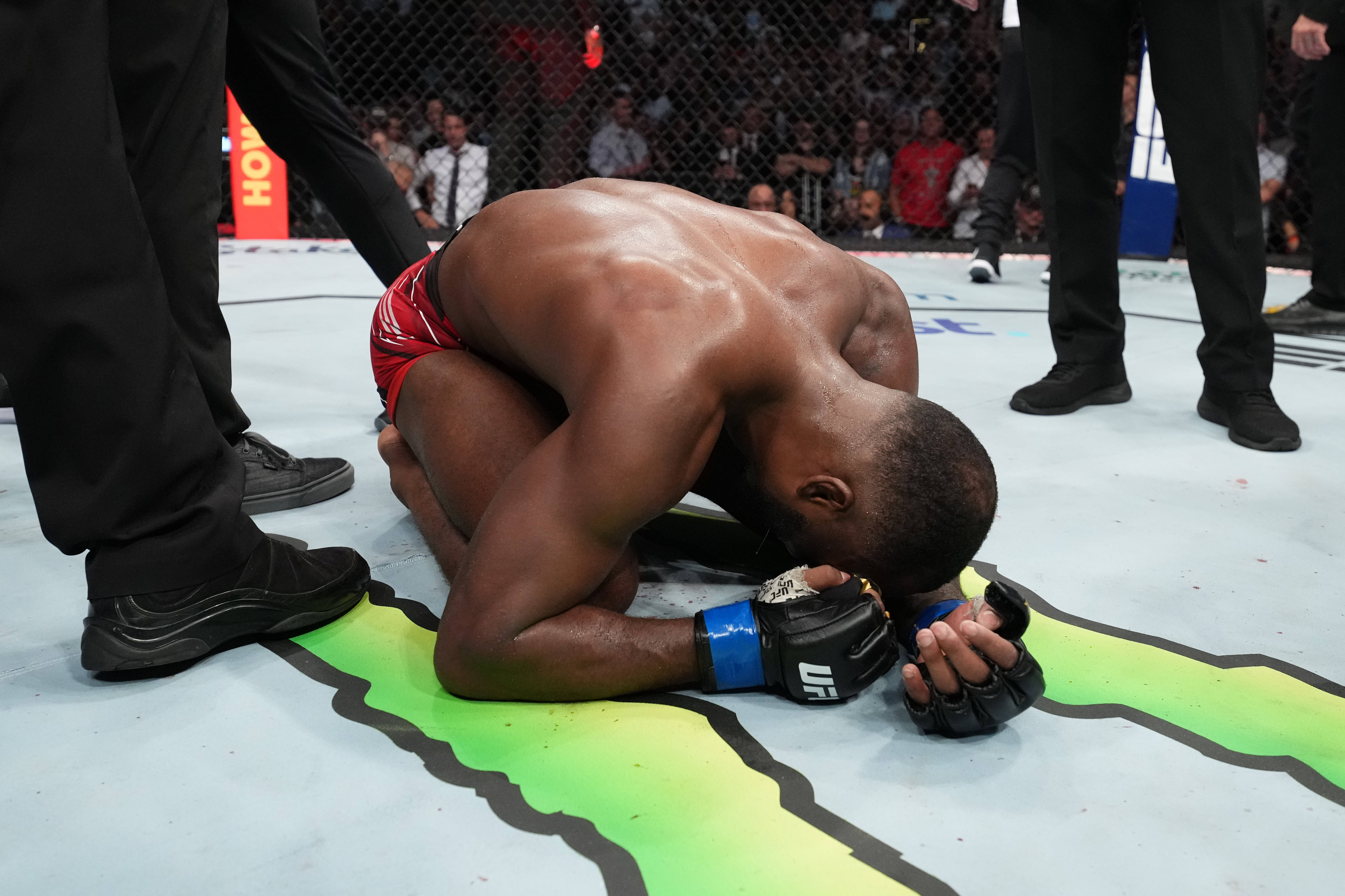 MMA 桌布 壁紙 — 一名肌肉發達的戰士在UFC八角籠墊上跪地失敗，官員們站在附近。