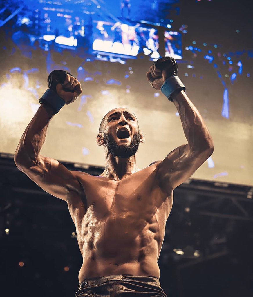 MMA 桌布 壁紙 — 一名肌肉發達的戰士在明亮的舞台燈光和五彩紙屑下，高舉拳頭發出勝利的咆哮。