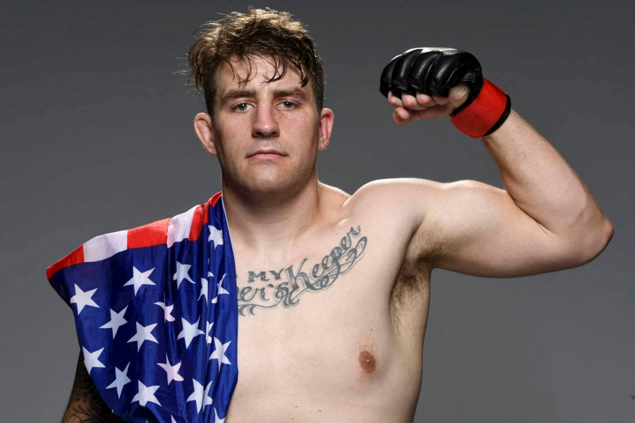 UFC 桌布 壁紙 — 一名肌肉發達的戰士在灰色工作室背景下，披著美國國旗展示二頭肌。