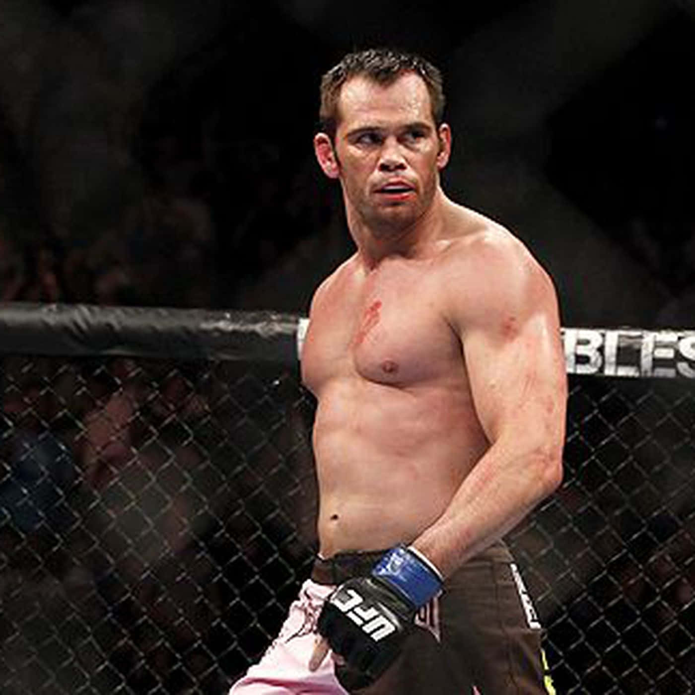 MMA 桌布 壁紙 — 一名肌肉發達的戰士胸口沾滿鮮血，在昏暗的八角籠內站立，剛剛經歷了一場殘酷的比賽。