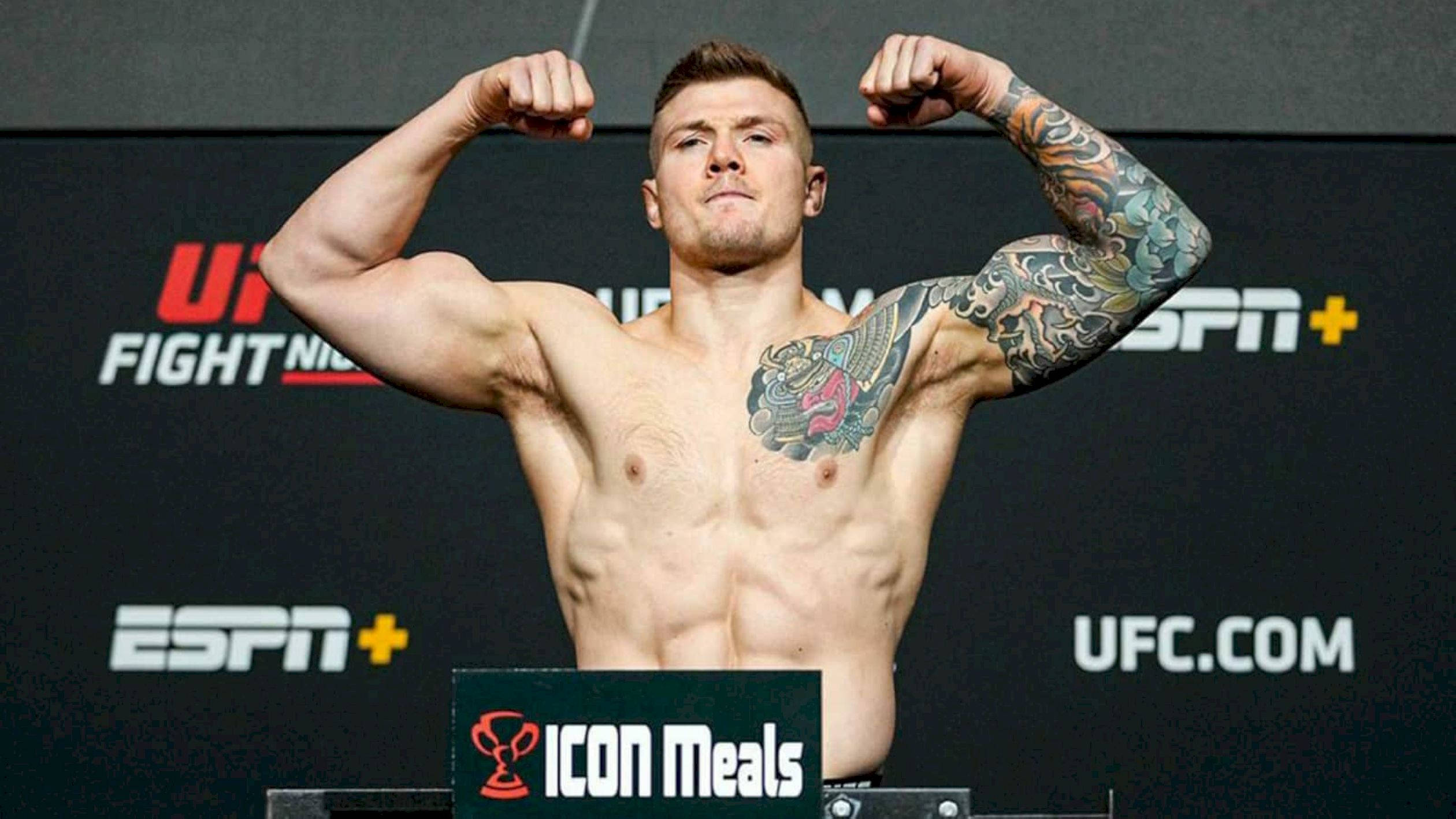 MMA 桌布 壁紙 — 一名肌肉發達的拳手在UFC稱重儀式上，於磅秤上屈起雙臂，身後有ESPN+品牌標誌。