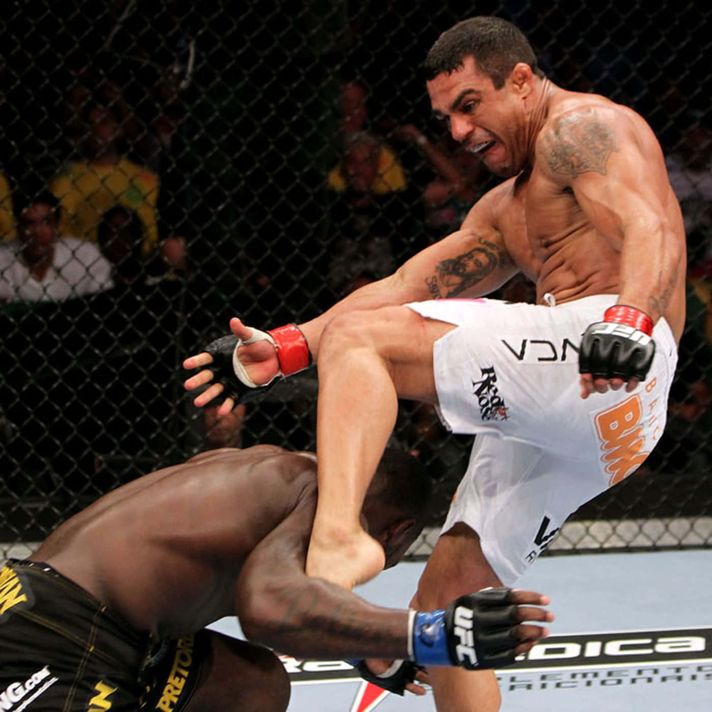 UFC 桌布 壁紙 — 一名肌肉發達的拳手在明亮的場館燈光下，於UFC八角籠中向對手踢出一記高踢。