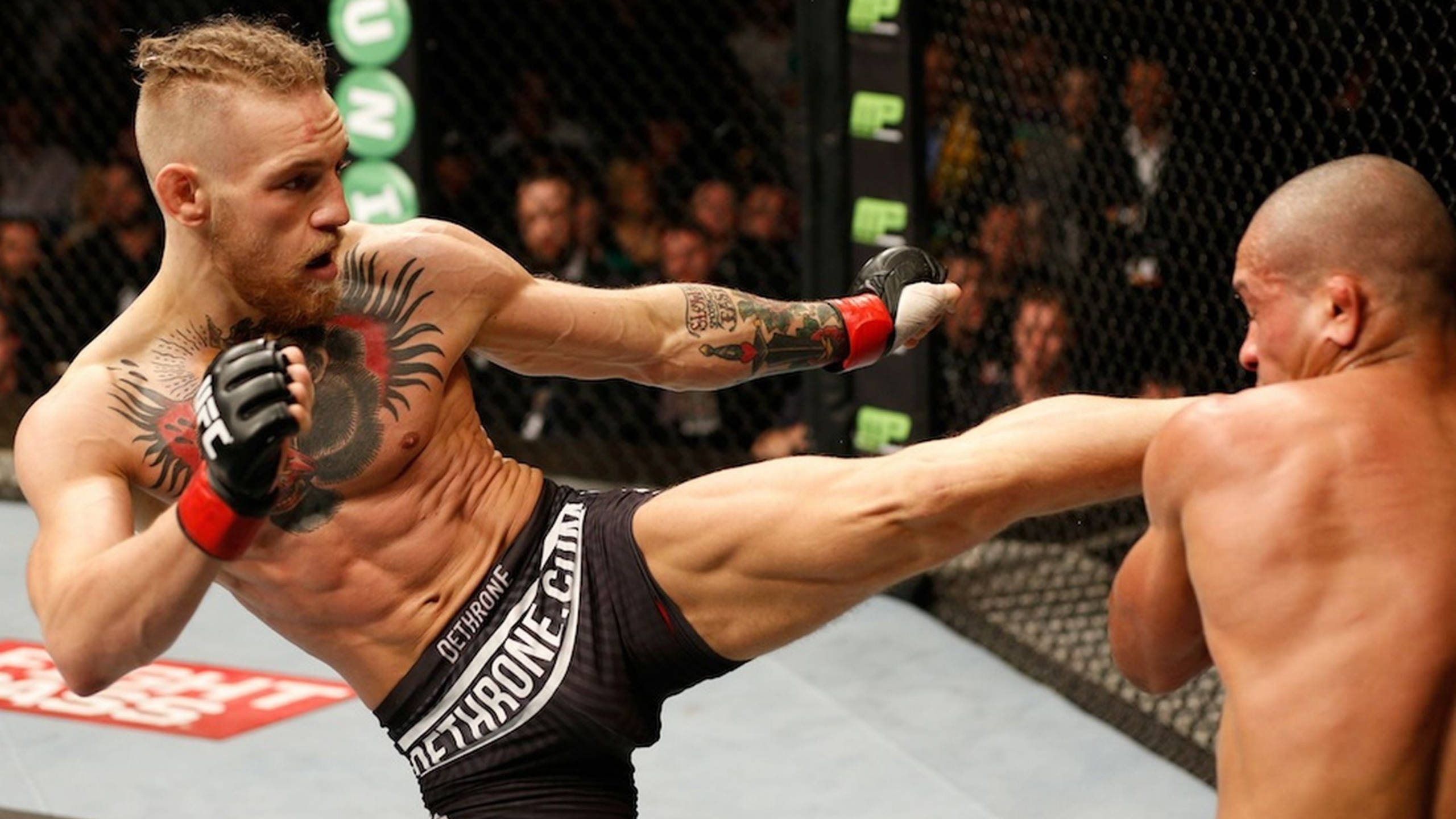 Mcgregor 桌布 壁紙 — 一名肌肉發達的拳手在明亮的場館燈光下，於UFC八角籠內向對手使出高踢。