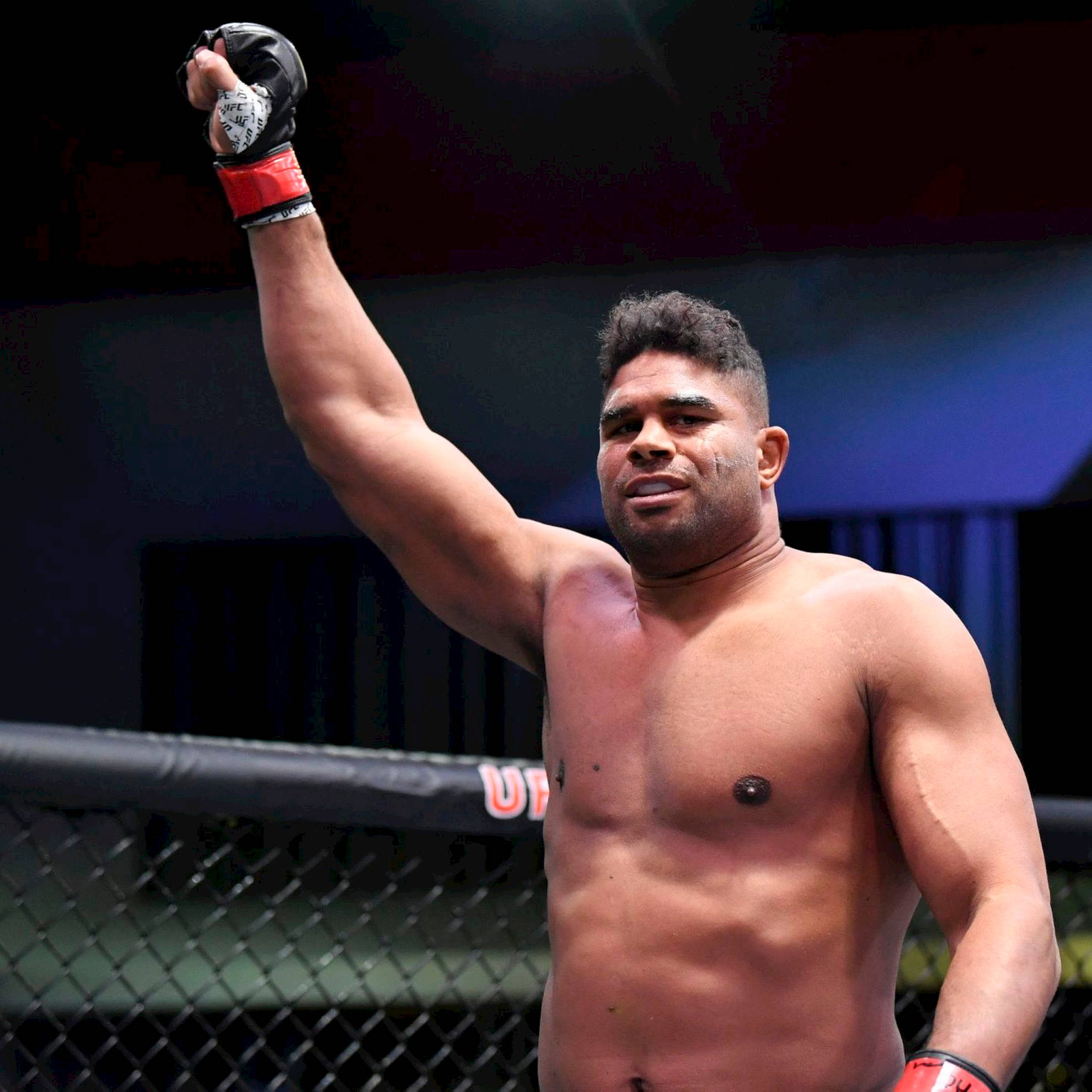 UFC 桌布 壁紙 — 一名肌肉發達的拳手在明亮的場館燈光下，於UFC八角籠內舉起戴著手套的拳頭慶祝勝利。