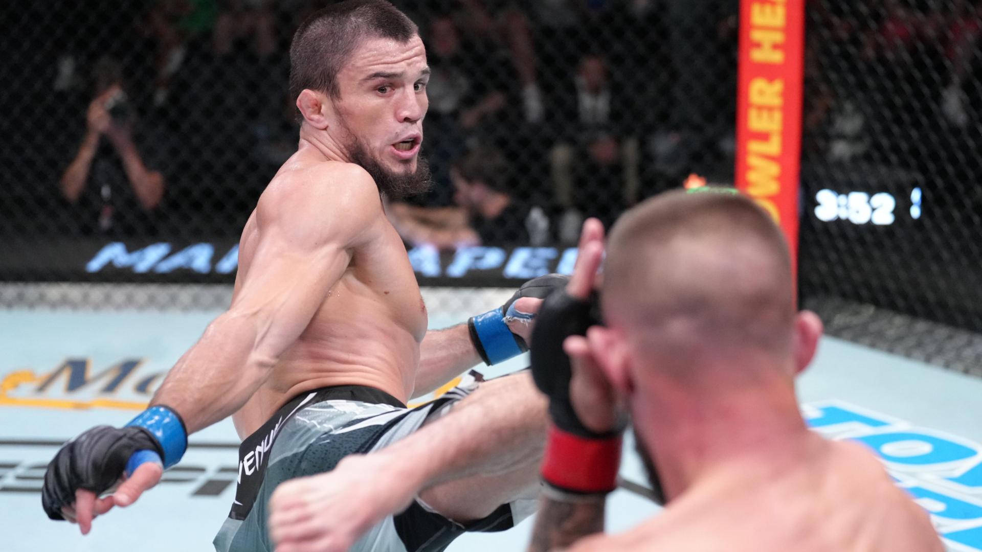 MMA 桌布 壁紙 — 一名肌肉發達的拳手在燈光明亮的MMA八角籠中踢出高踢，觀眾專注地觀看。