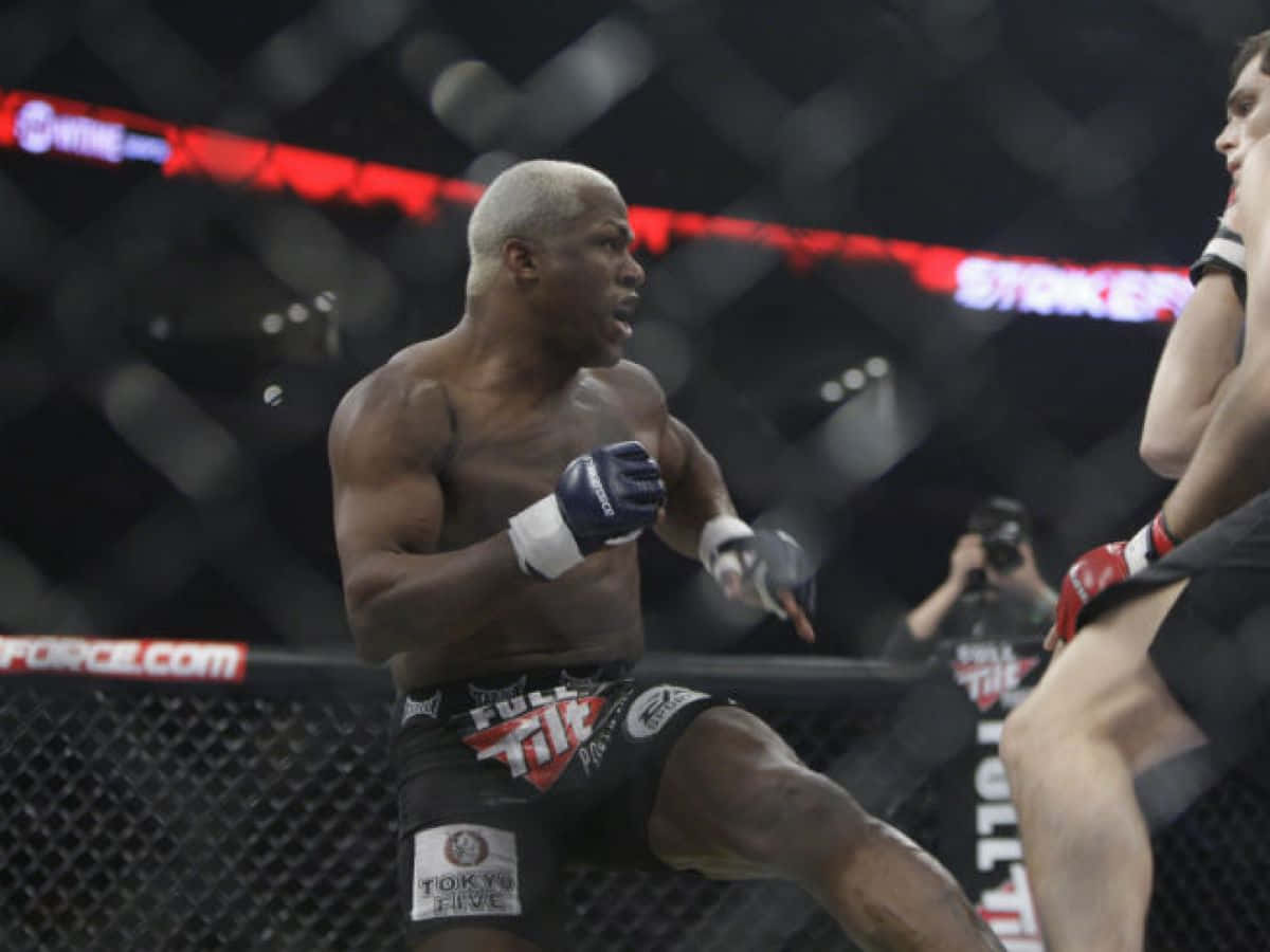 Fight 桌布 壁紙 — 一名肌肉發達的拳手在燈光昏暗、帶有紅色燈光和模糊觀眾的MMA八角籠內發出強力踢擊。