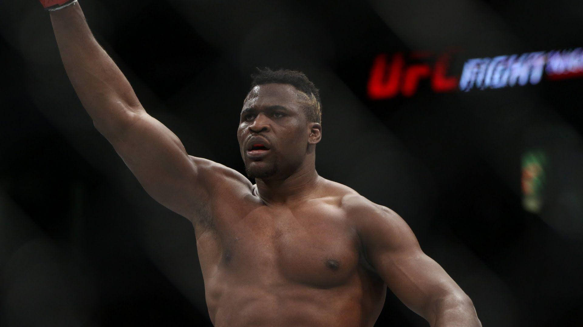 MMA 桌布 壁紙 — 一名肌肉發達的拳手在燈光昏暗的UFC八角籠內勝利地高舉手臂。