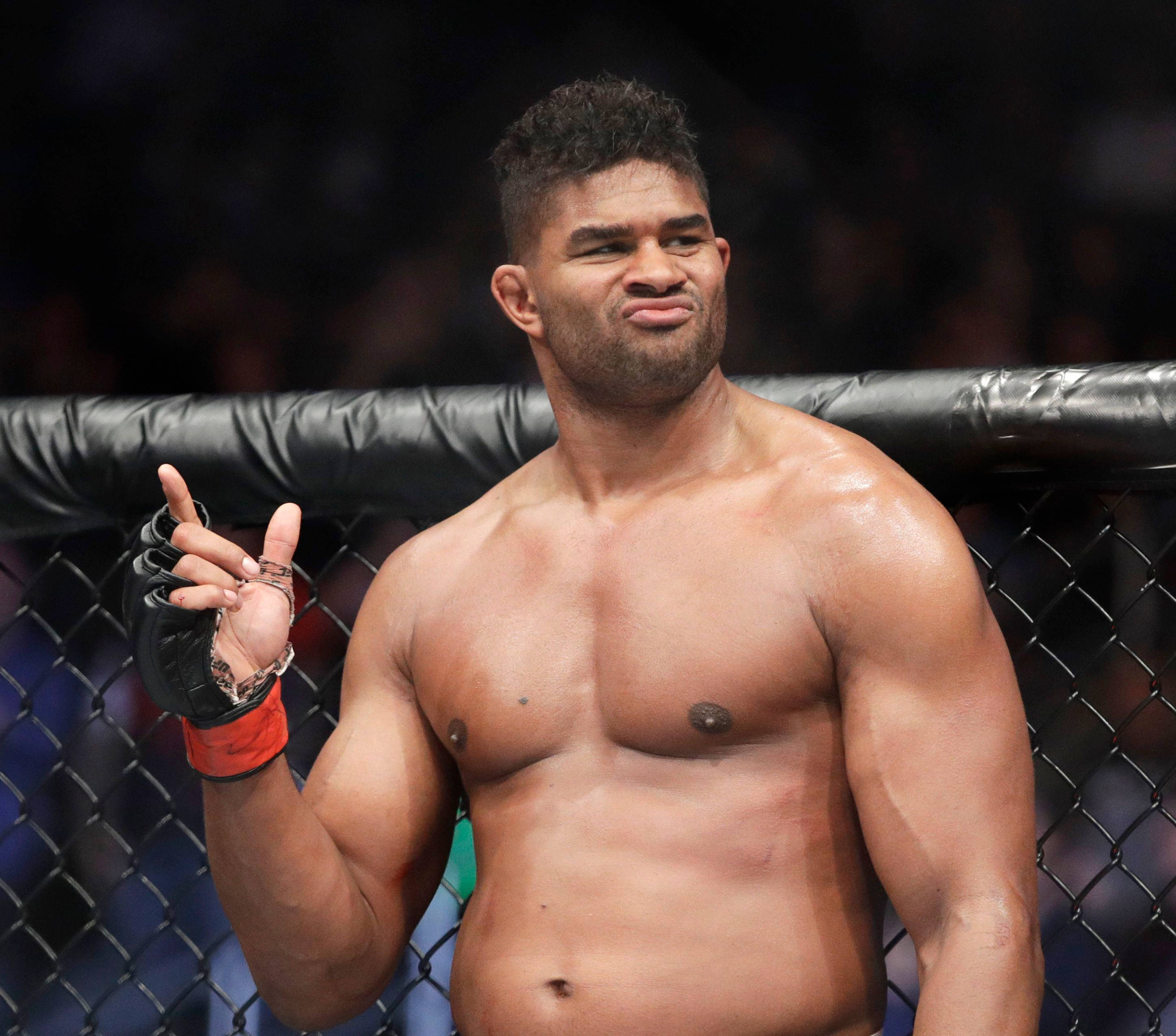 UFC 桌布 壁紙 — 一名肌肉發達的拳手在鐵籠內，於場館燈光下自信地微笑並做出和平手勢。