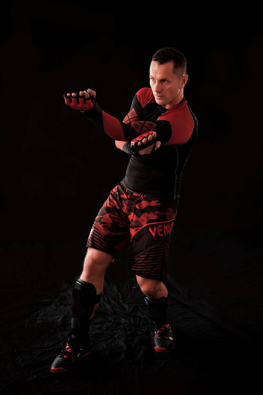 martial arts 桌布 壁紙 — 一名肌肉發達的男子身穿紅黑運動裝備，在黑暗的攝影棚背景下擺出強有力的戰鬥姿勢。