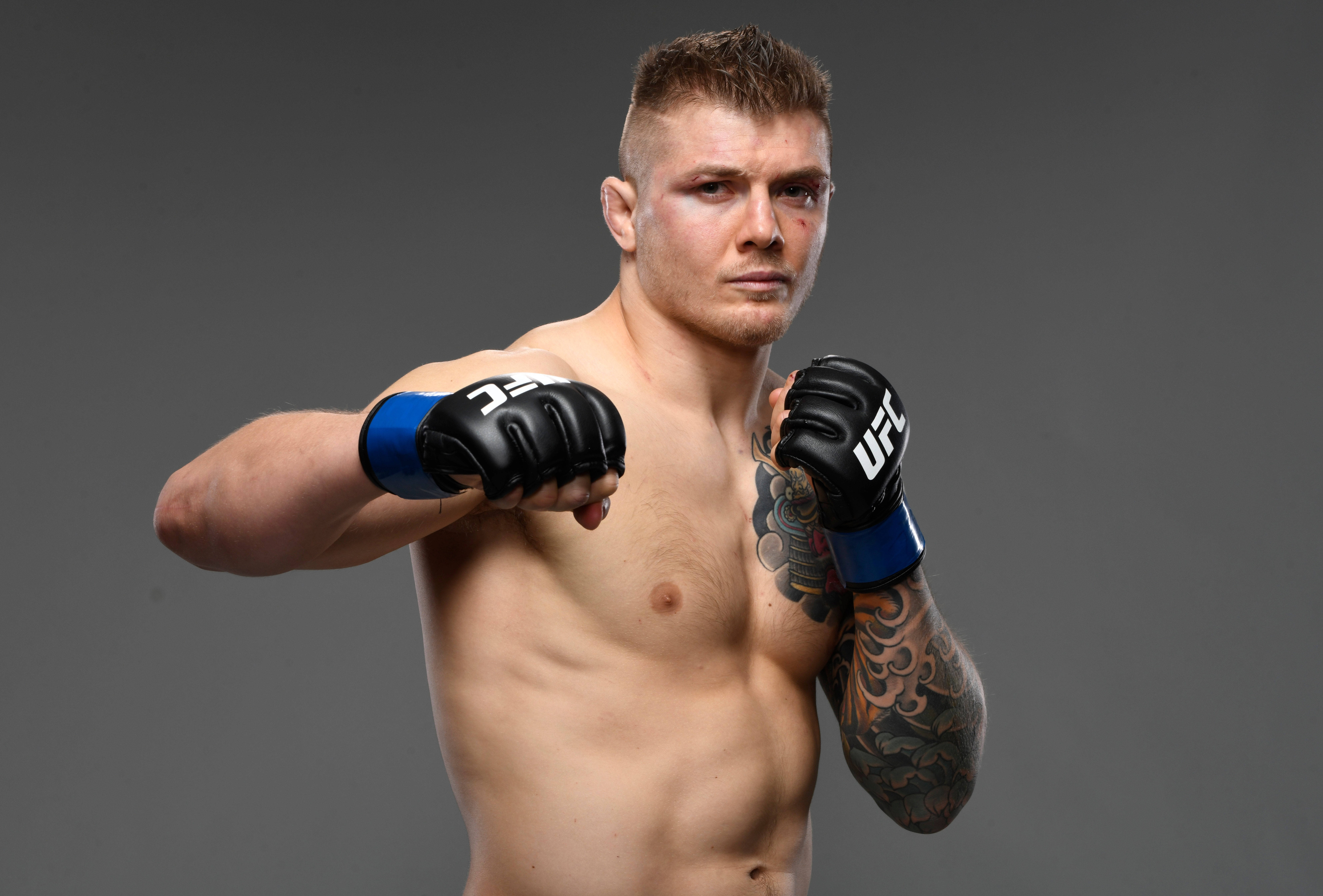 UFC 桌布 壁紙 — 一名肌肉發達的男性拳手戴著黑色和藍色的UFC手套，在純灰色工作室背景前擺出專注姿勢。