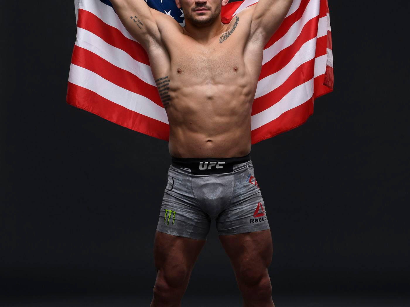 Michael Chandler 桌布 壁紙 — 一名肌肉發達的男性拳手穿著UFC短褲，在黑暗的攝影棚背景下高舉美國國旗。