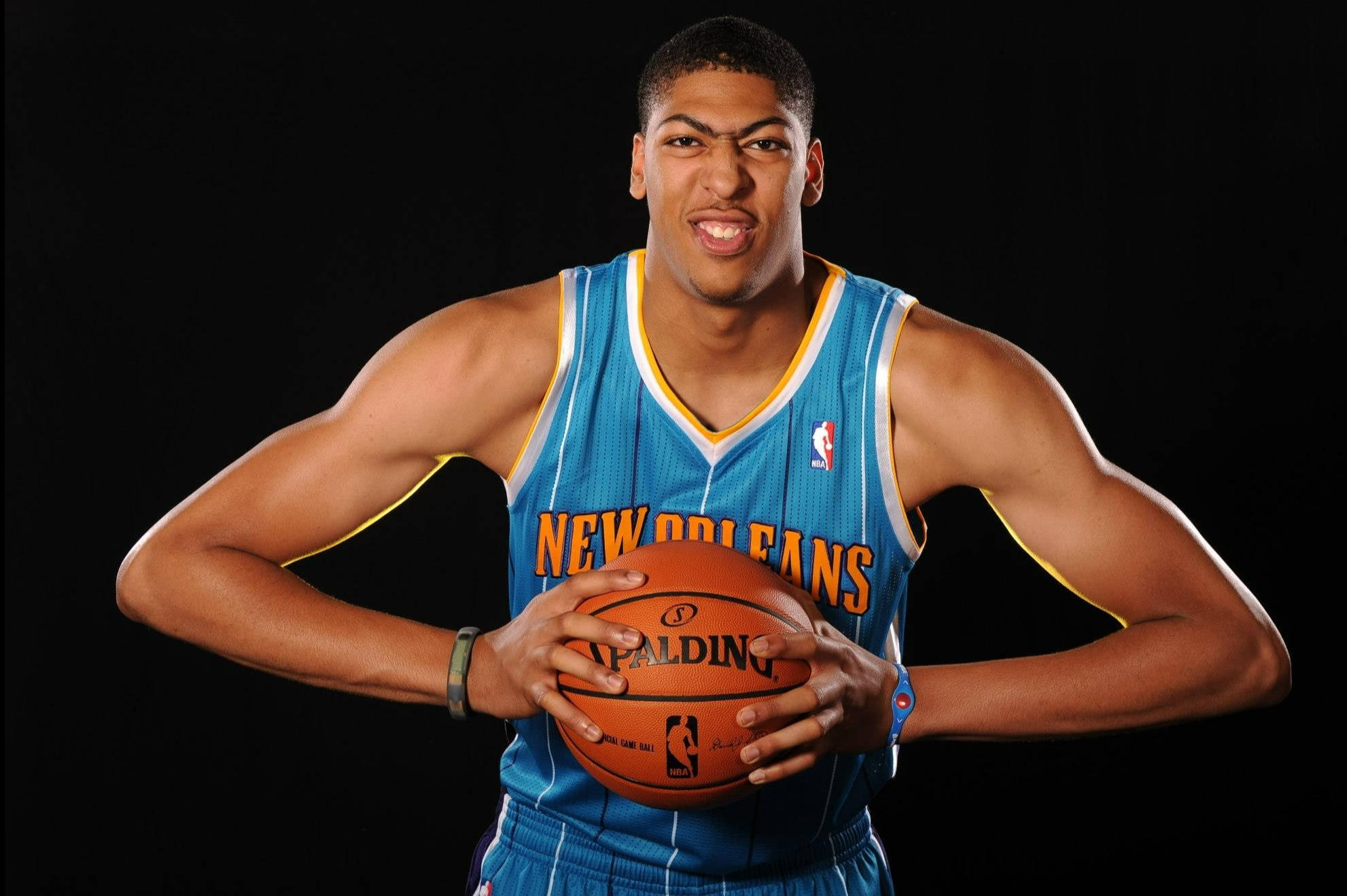 Anthony Davis 桌布 壁紙 — 一名肌肉發達的籃球運動員身穿紐奧良球衣，在黑色背景前拿著 Spalding 球咧嘴笑。