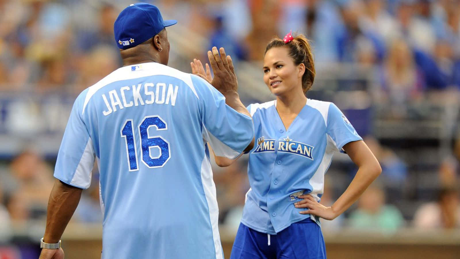 足球 桌布 壁紙 — 一名背上有「JACKSON 16」的棒球運動員在體育館與一名穿著淺藍色制服、微笑的女性運動員擊掌。