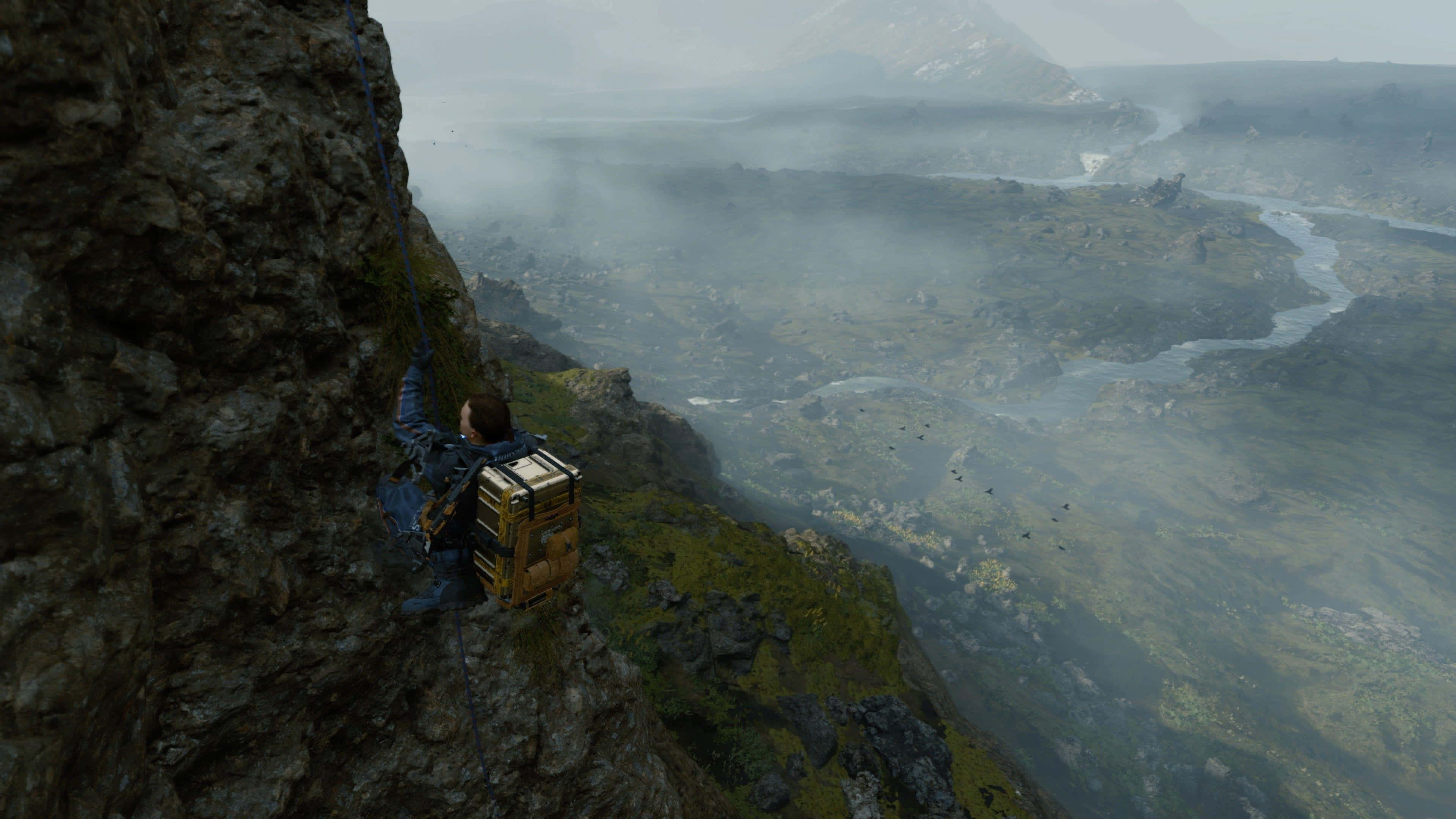 Death Stranding Pc 桌布 壁紙 — 一名背著大背包的登山者正在攀登霧濛濛的懸崖，俯瞰著一個擁有蜿蜒河流和遠山的廣闊山谷。