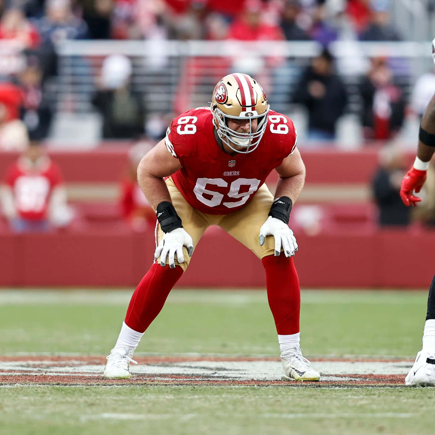 Mike Mcglinchey 桌布 壁紙 — 一名舊金山49人美式足球員身穿紅、金、白色球衣，在球場上低蹲準備行動。