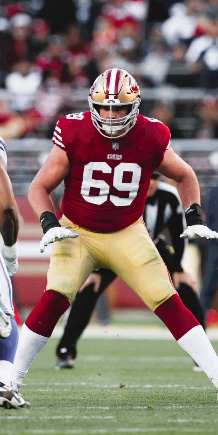 Mike Mcglinchey 桌布 壁紙 — 一名舊金山四九人隊的足球員，身穿紅金色69號球衣，在比賽期間準備就緒，站在綠色球場上。