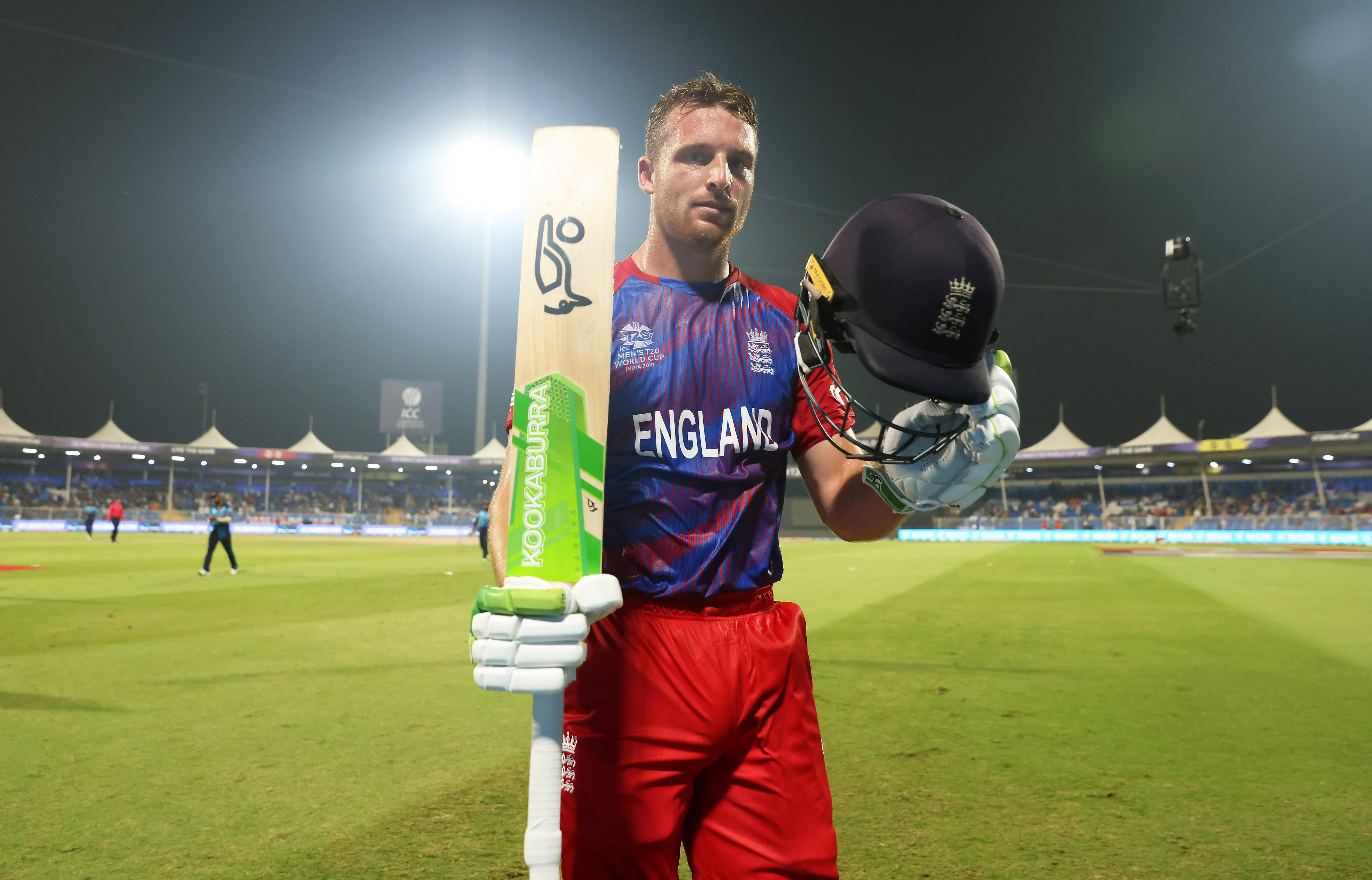 jos buttler 桌布 壁紙 — 一名英格蘭板球運動員在夜間站在有泛光燈照明的體育場地上，手持球棒和頭盔。