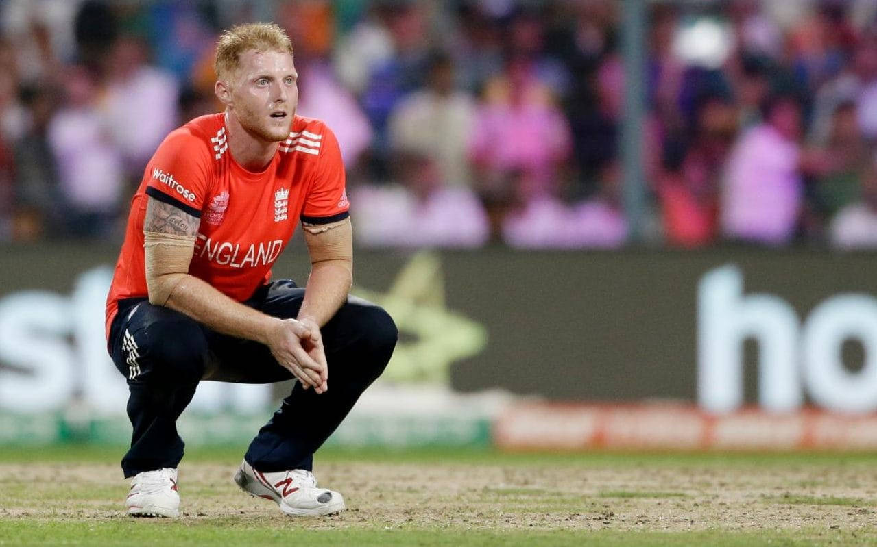 Ben Stokes 桌布 壁紙 — 一名英格蘭板球運動員在球場燈光下，背景有模糊的觀眾，專注地蹲在草地上。