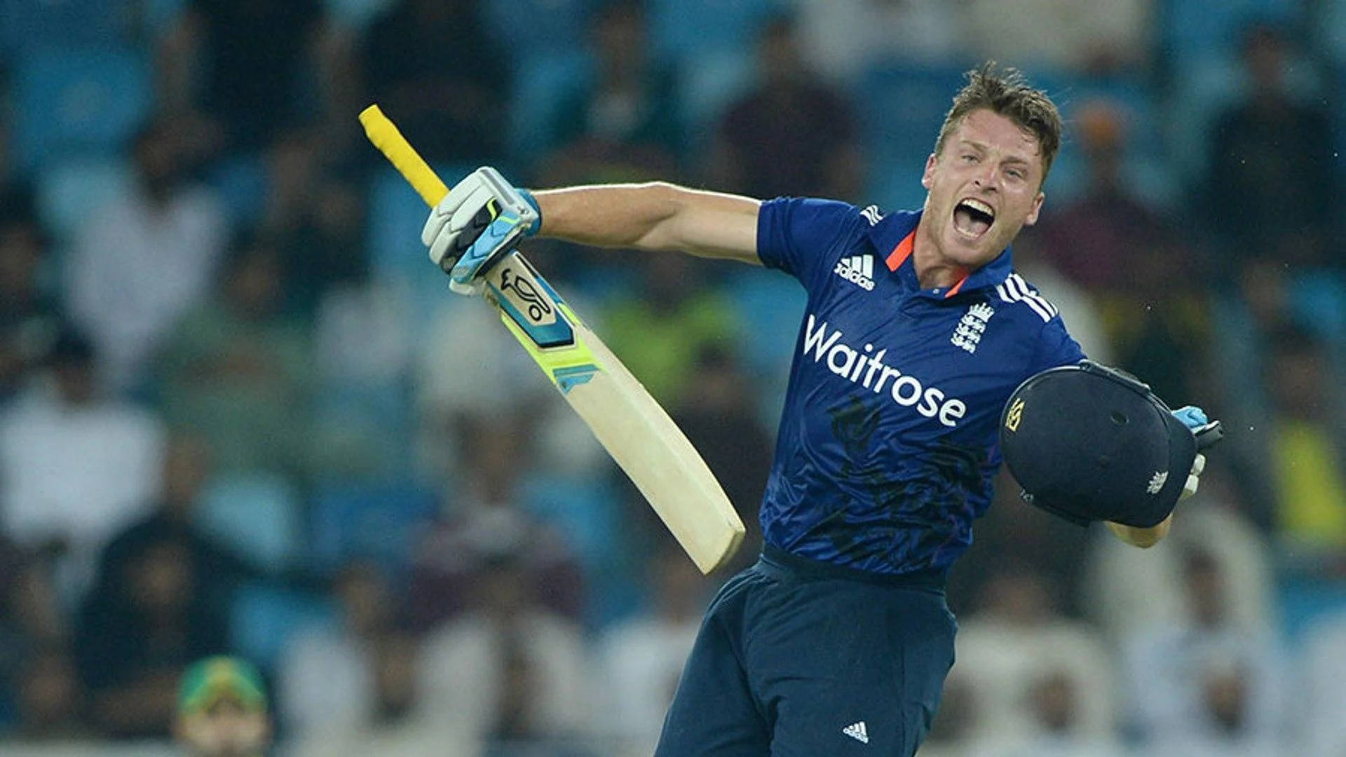 jos buttler 桌布 壁紙 — 一名英格蘭板球運動員在體育場燈光下高舉球棒、手持頭盔，勝利慶祝。