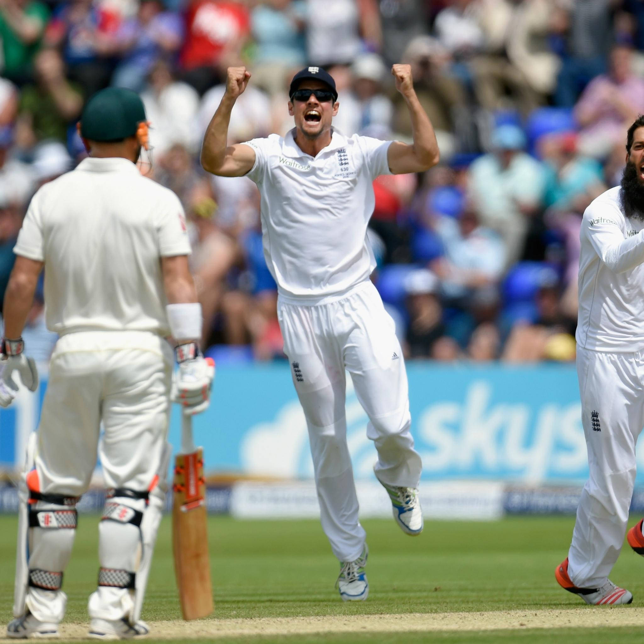England Cricket 桌布 壁紙 — 一名英格蘭板球運動員高舉拳頭勝利跳躍，隊友在陽光明媚的綠色球場上慶祝。