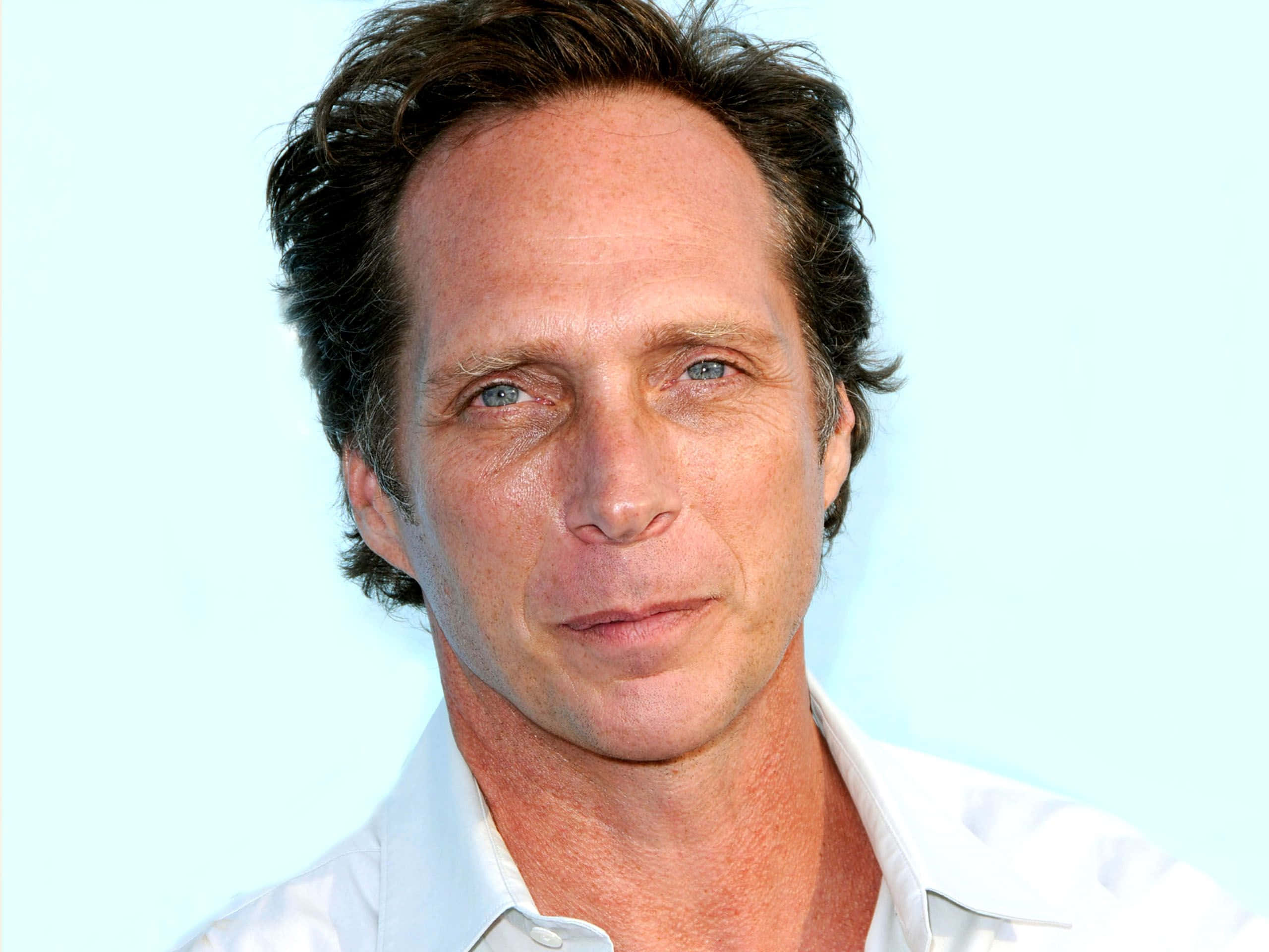 William Fichtner 桌布 壁紙 — 一名藍眼睛、深色頭髮的男子穿著白色襯衫，在淺藍色背景前的特寫肖像。