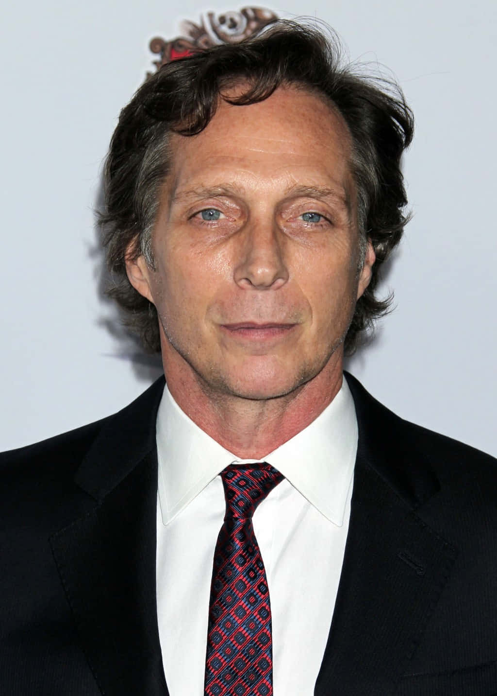 William Fichtner 桌布 壁紙 — 一名藍眼睛、深色頭髮的男子穿著黑色西裝、白襯衫和圖案紅色領帶的特寫肖像。