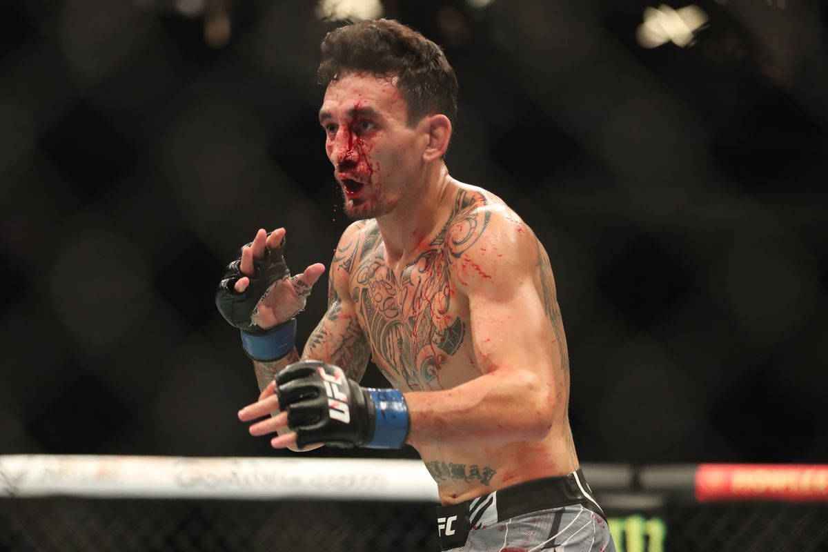 UFC 桌布 壁紙 — 一名血跡斑斑、身上有刺青的拳手在UFC八角籠中高舉手臂，展現勝利的強烈情感。