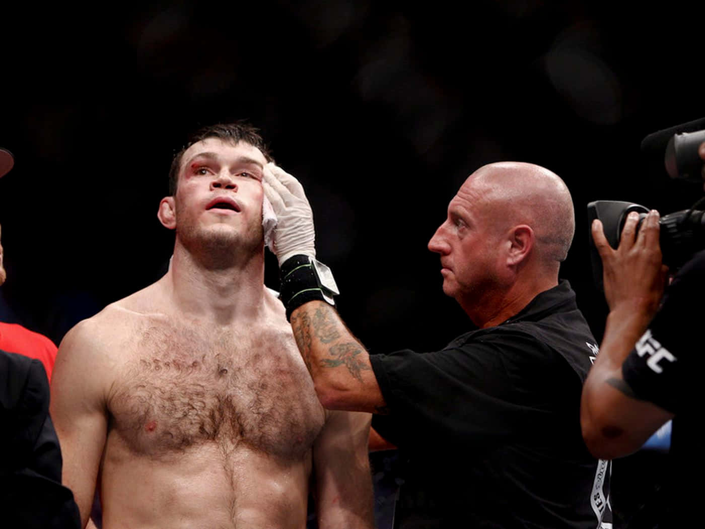 UFC 桌布 壁紙 — 一名血跡斑斑的MMA拳手在明亮的場館燈光下，於一場殘酷的比賽後接受醫護人員的治療。