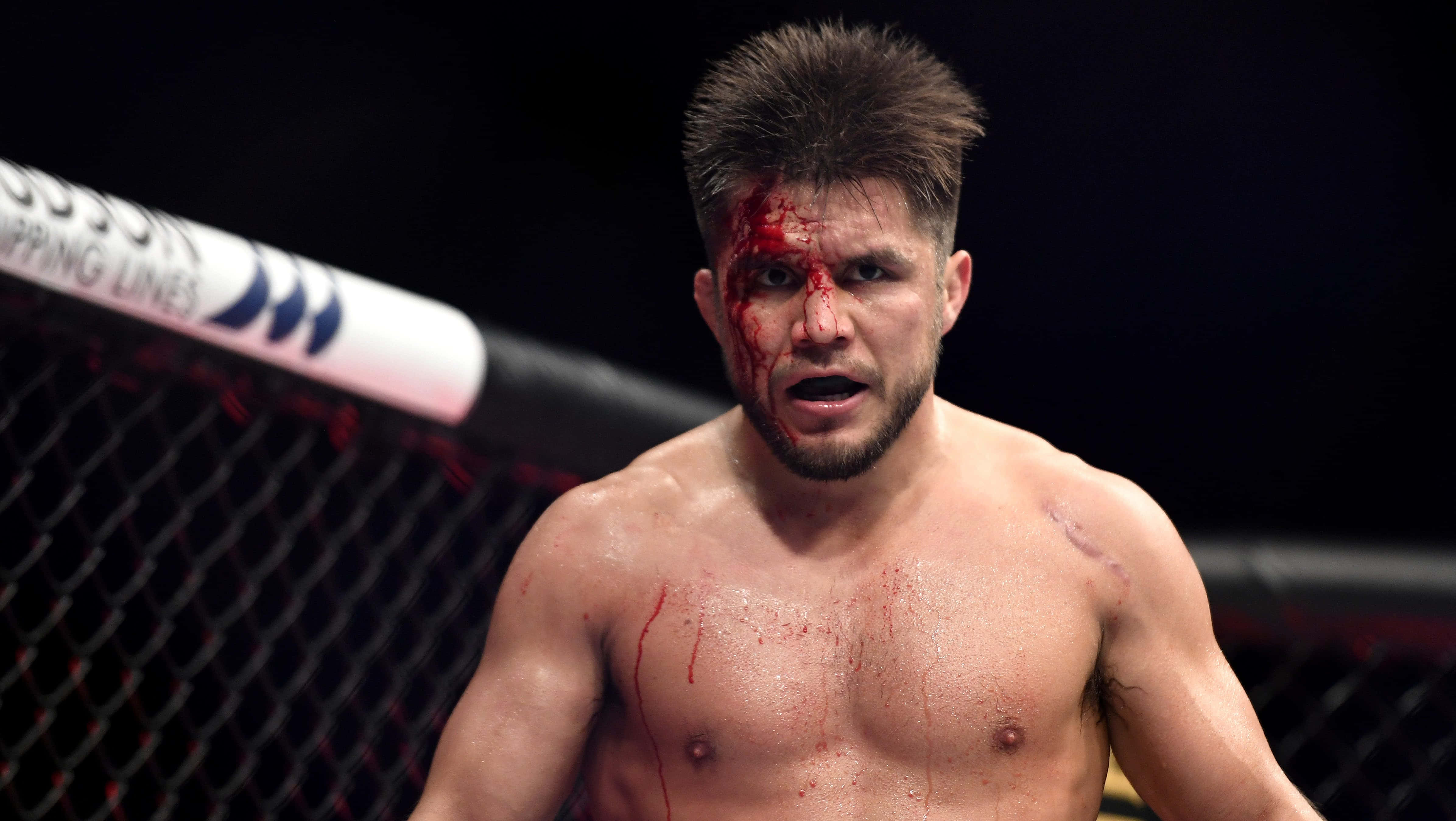 UFC 桌布 壁紙 — 一名血跡斑斑的MMA拳手在明亮的場館燈光下，從八角籠內凝視著。