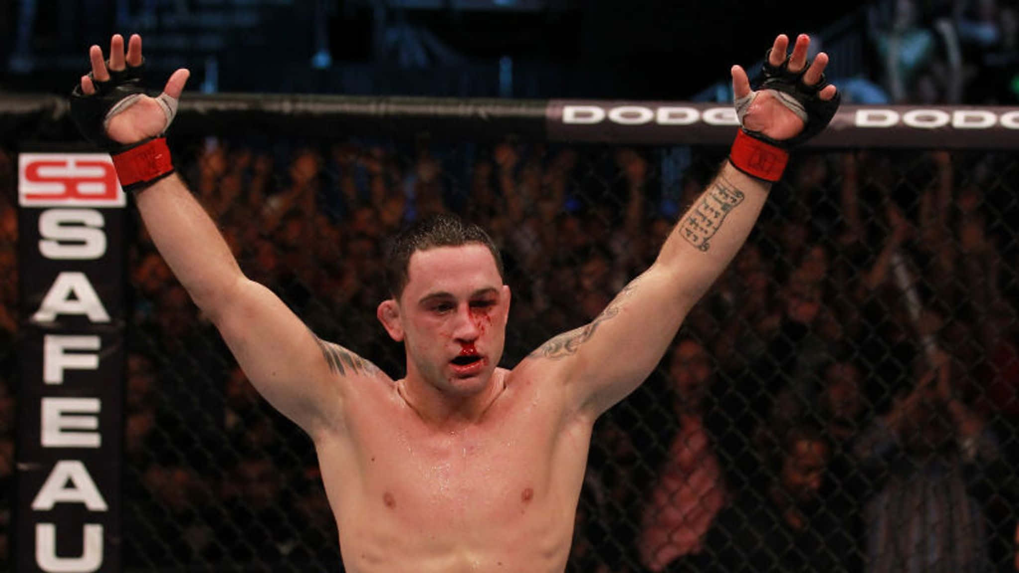 UFC 桌布 壁紙 — 一名血跡斑斑的MMA拳手在籠內高舉雙臂慶祝勝利，身後是歡呼的人群。
