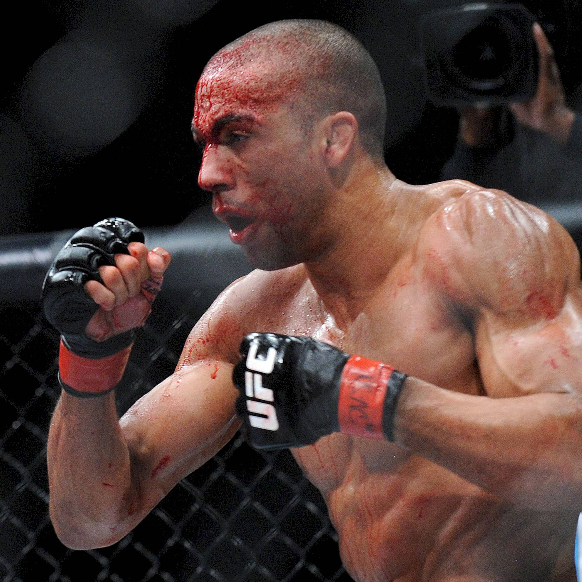 UFC 桌布 壁紙 — 一名血跡斑斑的UFC拳手在八角籠中咆哮，汗水和深紅色條紋佈滿他的臉部和軀幹。