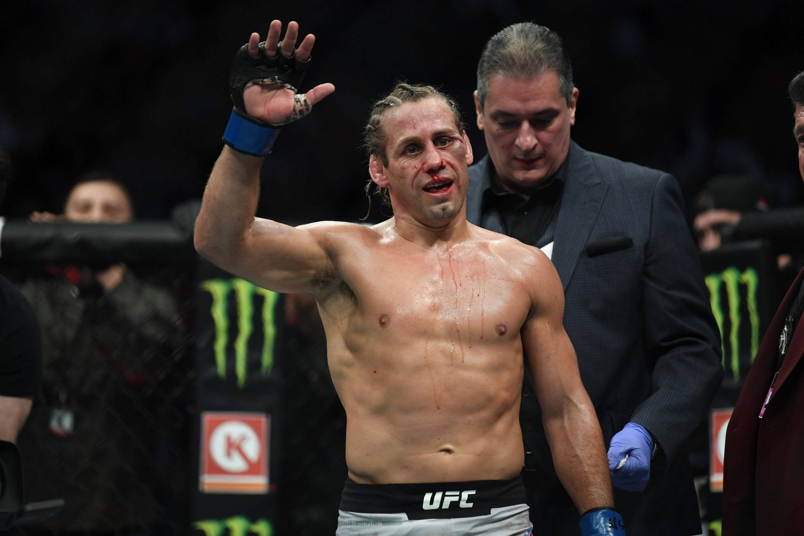 MMA 桌布 壁紙 — 一名血跡斑斑的UFC拳手在明亮的場館燈光下，於八角籠內進行一場殘酷比賽後向粉絲揮手。