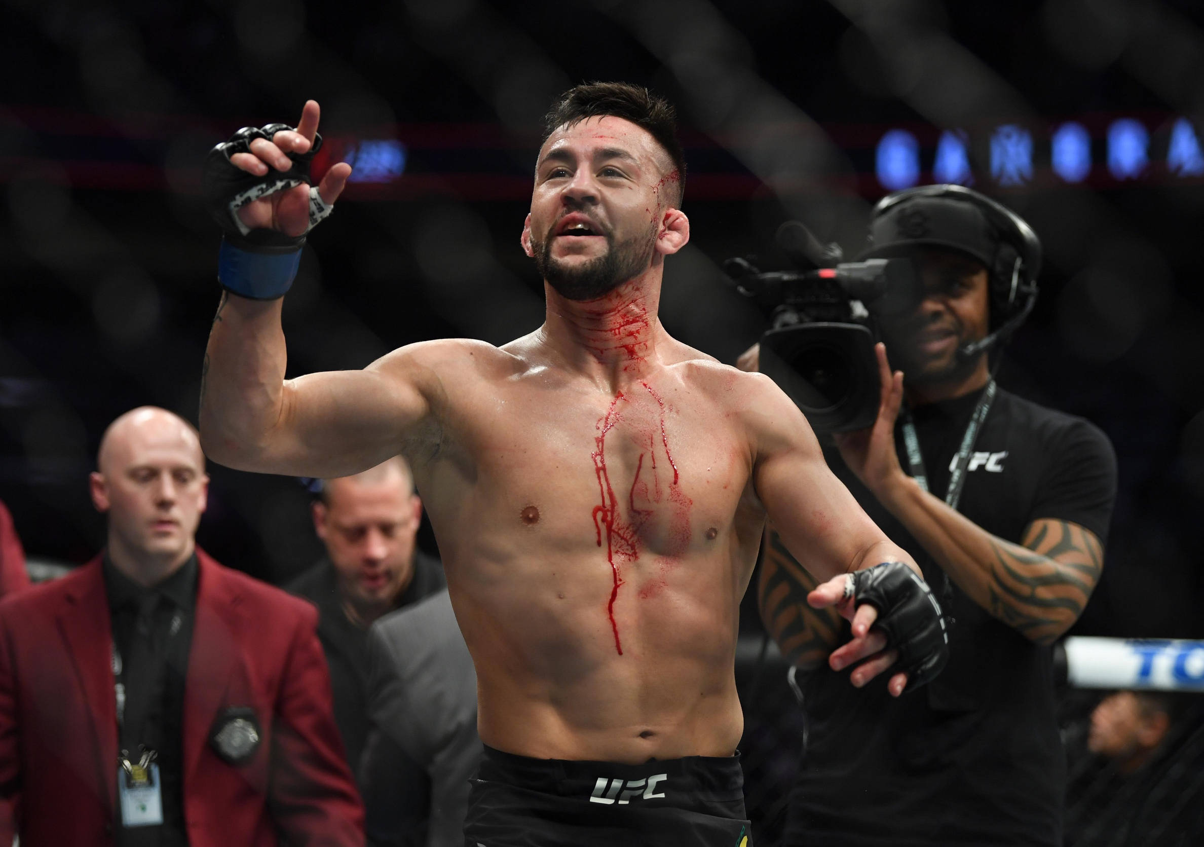 Champion 桌布 壁紙 — 一名血跡斑斑的UFC拳手在明亮的場館燈光下，於八角籠內勝利地高舉手臂。